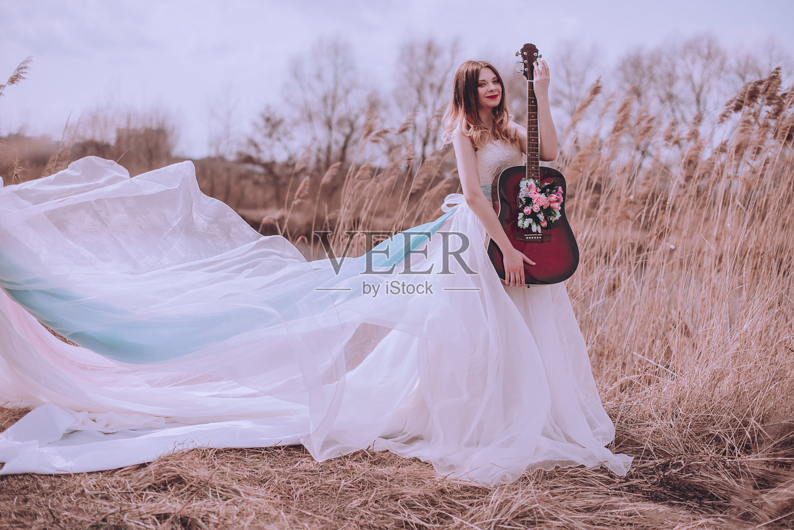 美丽浪漫的欧洲女孩与吉他与花里面，摆姿势在户外。音乐与自然的概念。春天的时间。照片摄影图片