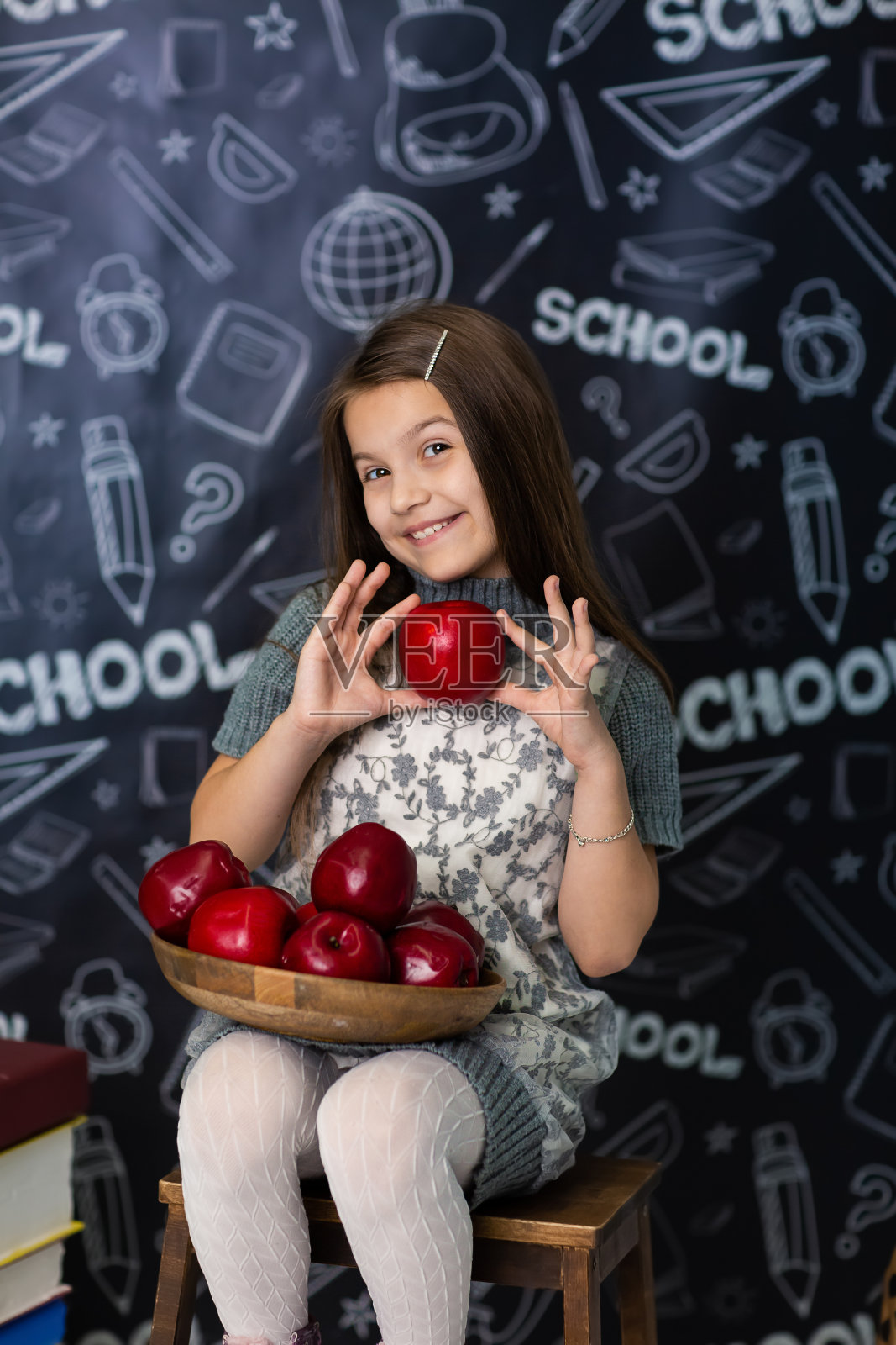 一个穿着灰色连衣裙的女孩坐在椅子上，手里拿着苹果块。她去上学照片摄影图片