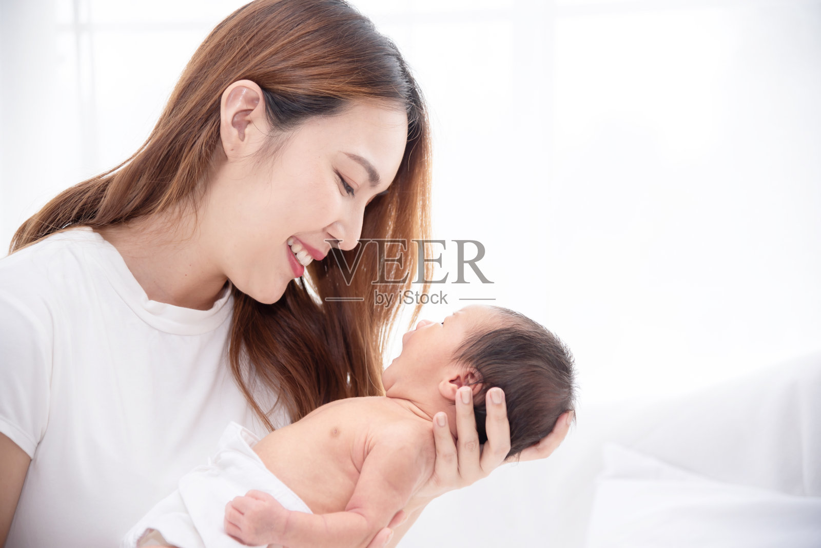 亚洲慈爱的妈妈在家里孕育她的新生婴儿。幸福的妈妈手里抱着熟睡的婴儿。母亲抱着一个月大的儿子。照片摄影图片