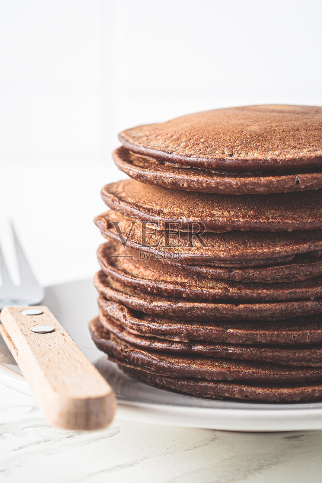 白色厨房里的白色盘子上堆着巧克力煎饼。照片摄影图片
