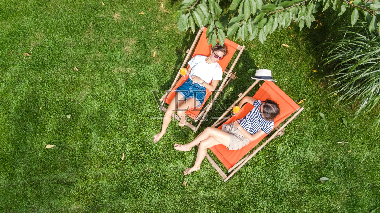 年轻女孩在夏日花园的草地上躺着日光浴躺椅，女性朋友在周末的绿色公园里享受户外的乐趣，从空中俯瞰照片摄影图片