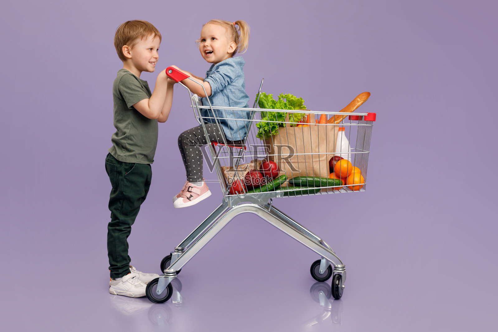 一个小男孩推着一个小女孩在购物车里。孤立的概念形象。“n照片摄影图片