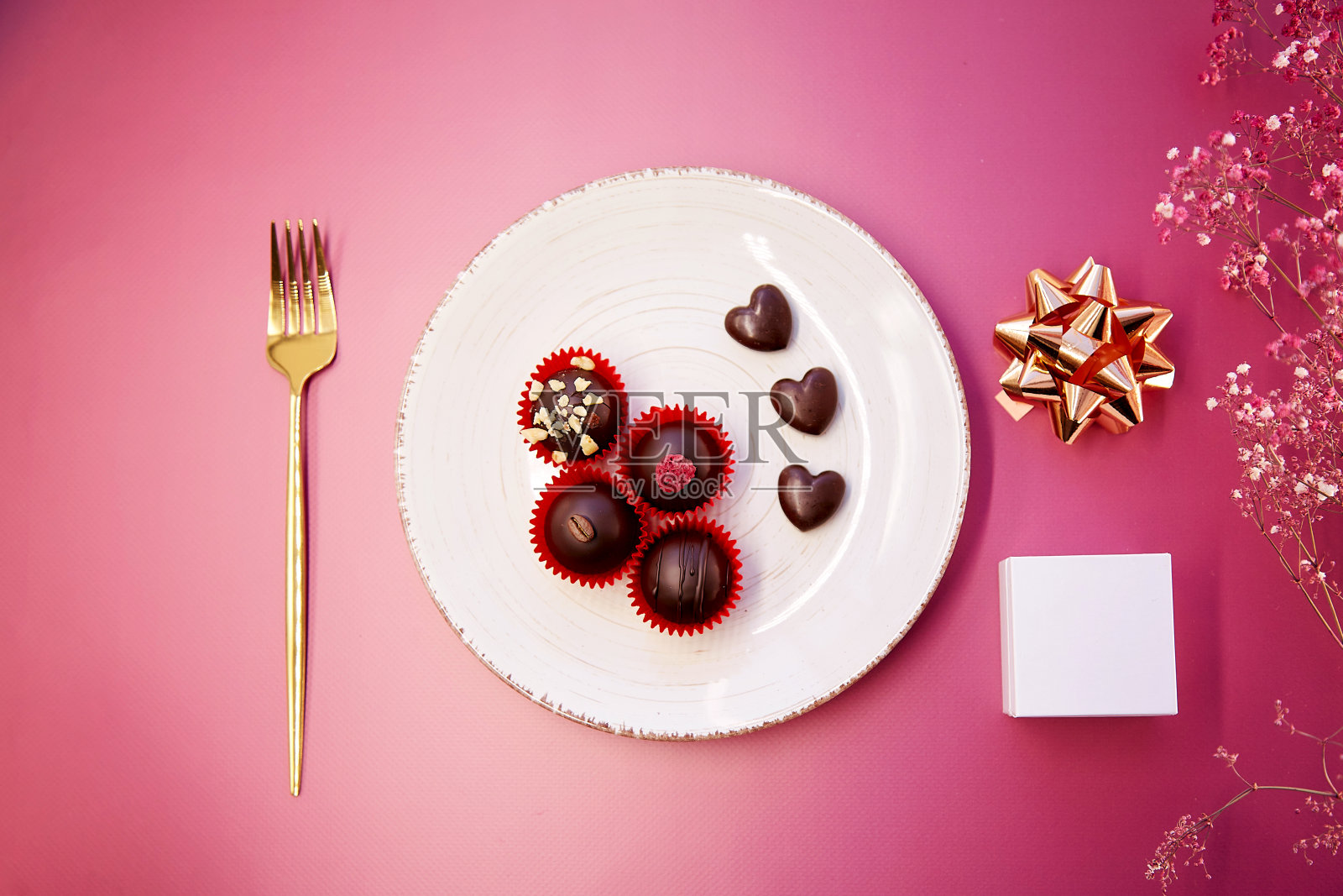 用叉子将心形手工巧克力糖放在盘子上。白盒子模拟创意礼物概念。前视图。浪漫晚餐的概念。粉红色的渐变背景照片摄影图片