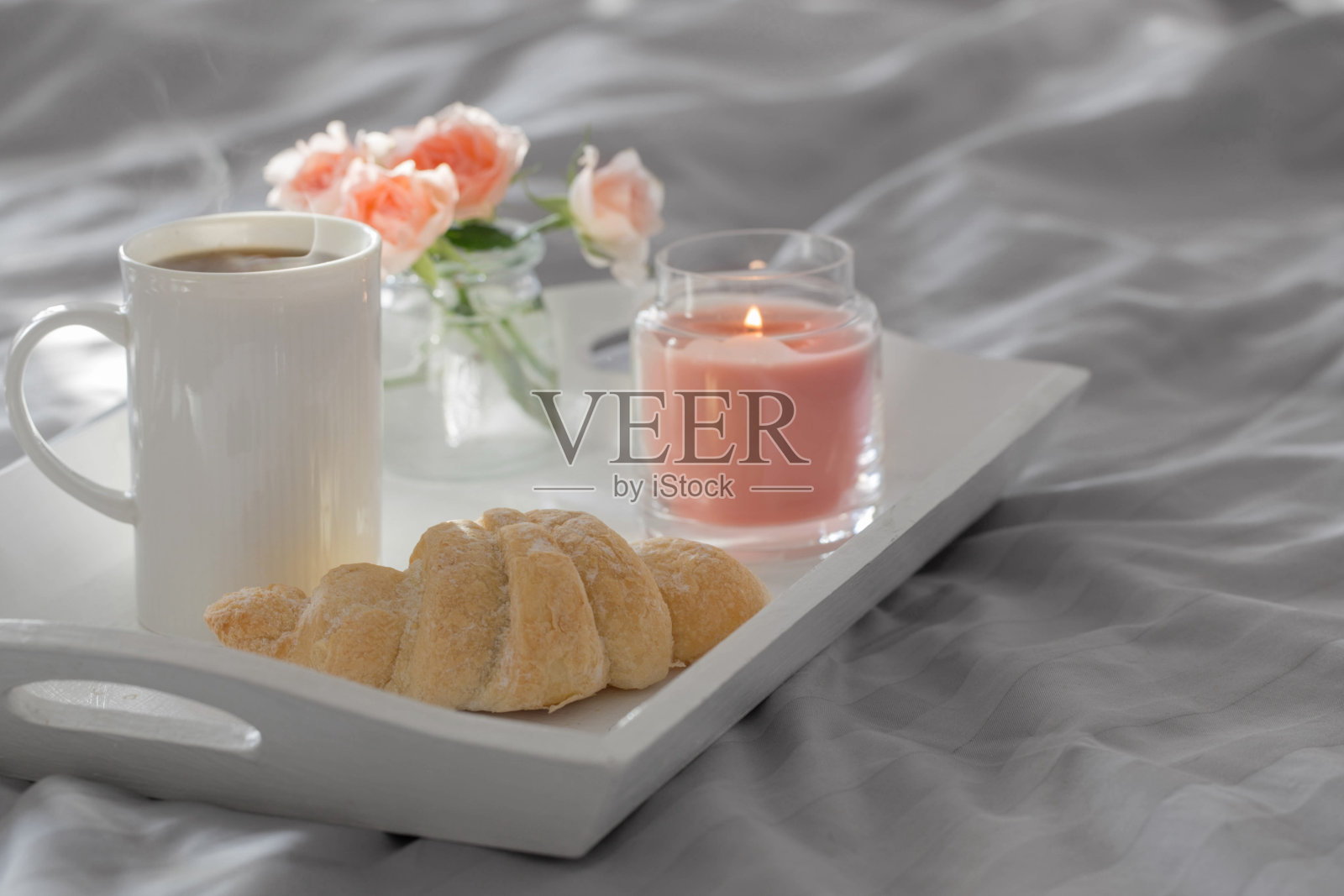 在卧室的床上喝杯咖啡，配上牛角面包和粉色玫瑰照片摄影图片