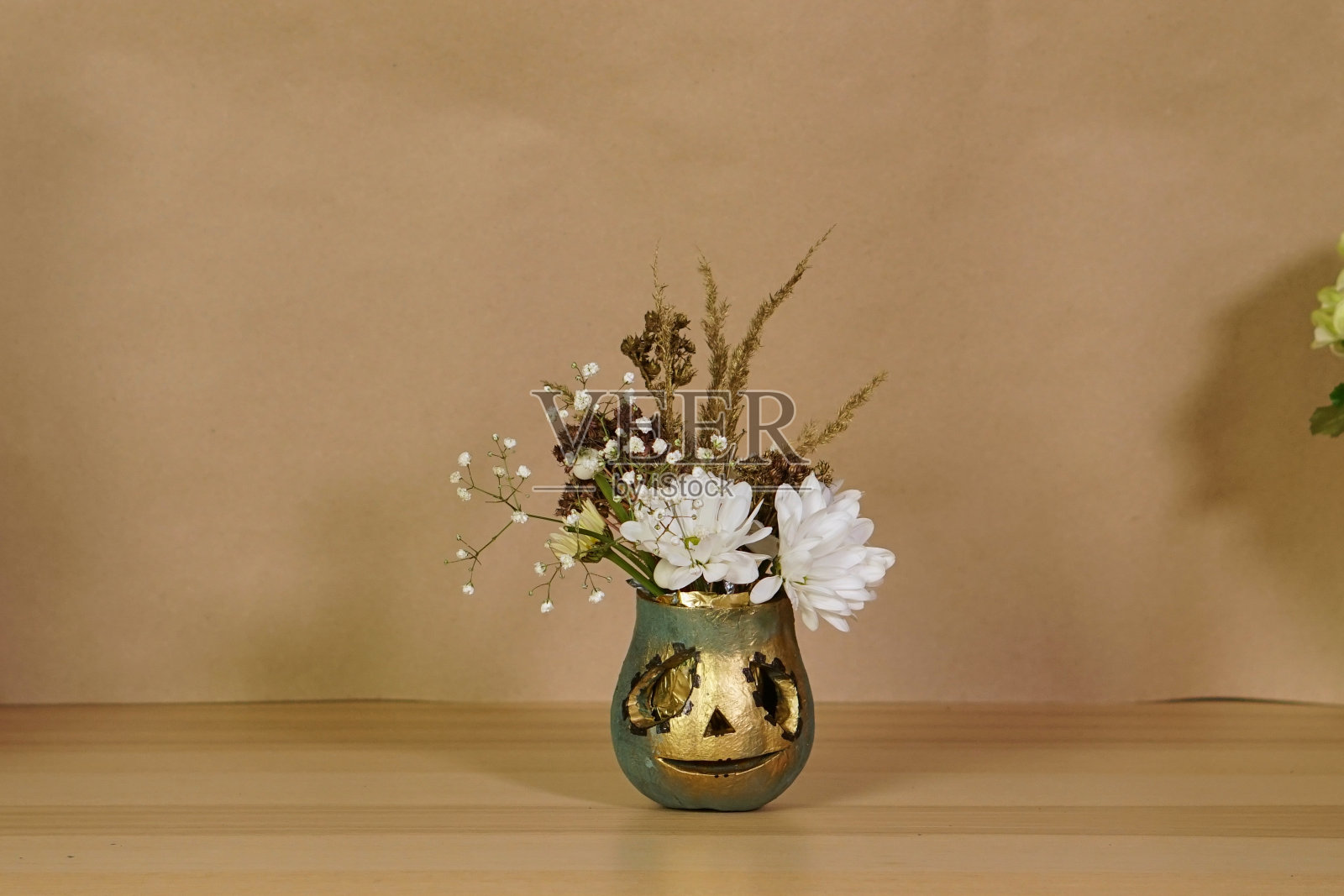 万圣节南瓜杰克与花在工艺背景。装饰鲜花和金色的南瓜。把南瓜的脸剪下来，用金色的颜料涂上。南瓜里的秋天花束。照片摄影图片