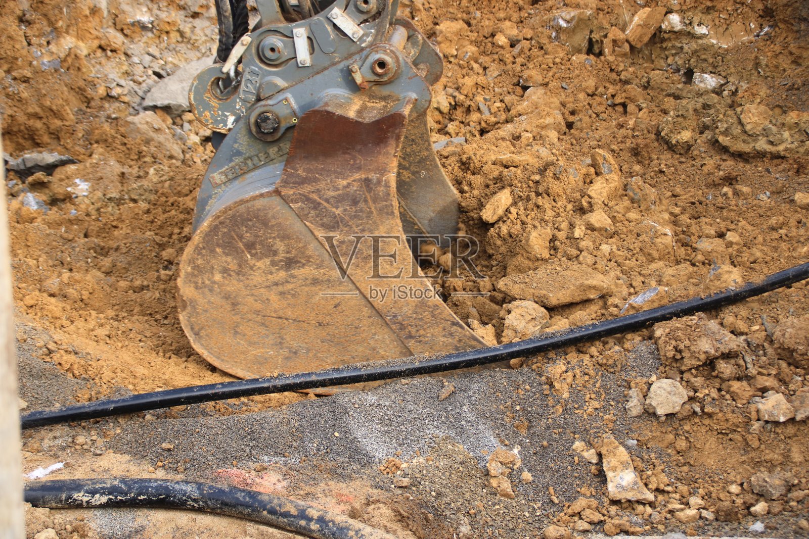 挖掘机的抓斗在电缆旁边的地面上挖掘照片摄影图片