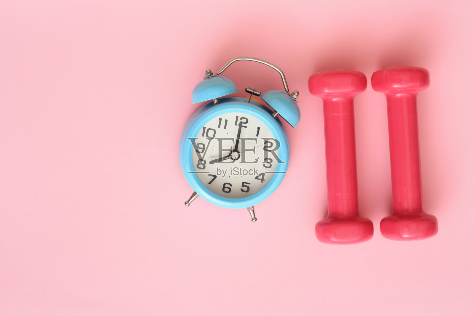 练习桌上粉红色背景的钟和哑铃的时间到了照片摄影图片