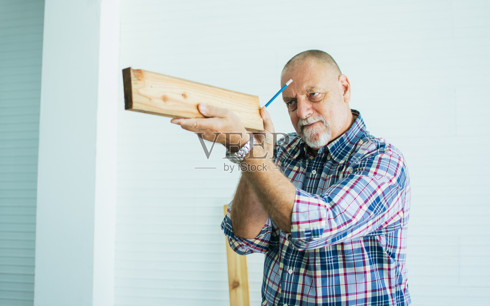 老年白种人快乐退休的老男性木工或木匠微笑着，穿着格子衬衫，量身打造DIY的木制家居模型。爱好,退休的概念。照片摄影图片