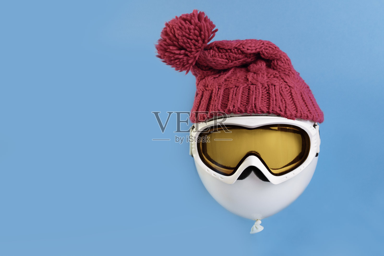 冬天的假期。蓝色背景上漂浮的气球，戴着滑雪面罩和冬季帽子。旅游与冬季运动的概念照片摄影图片
