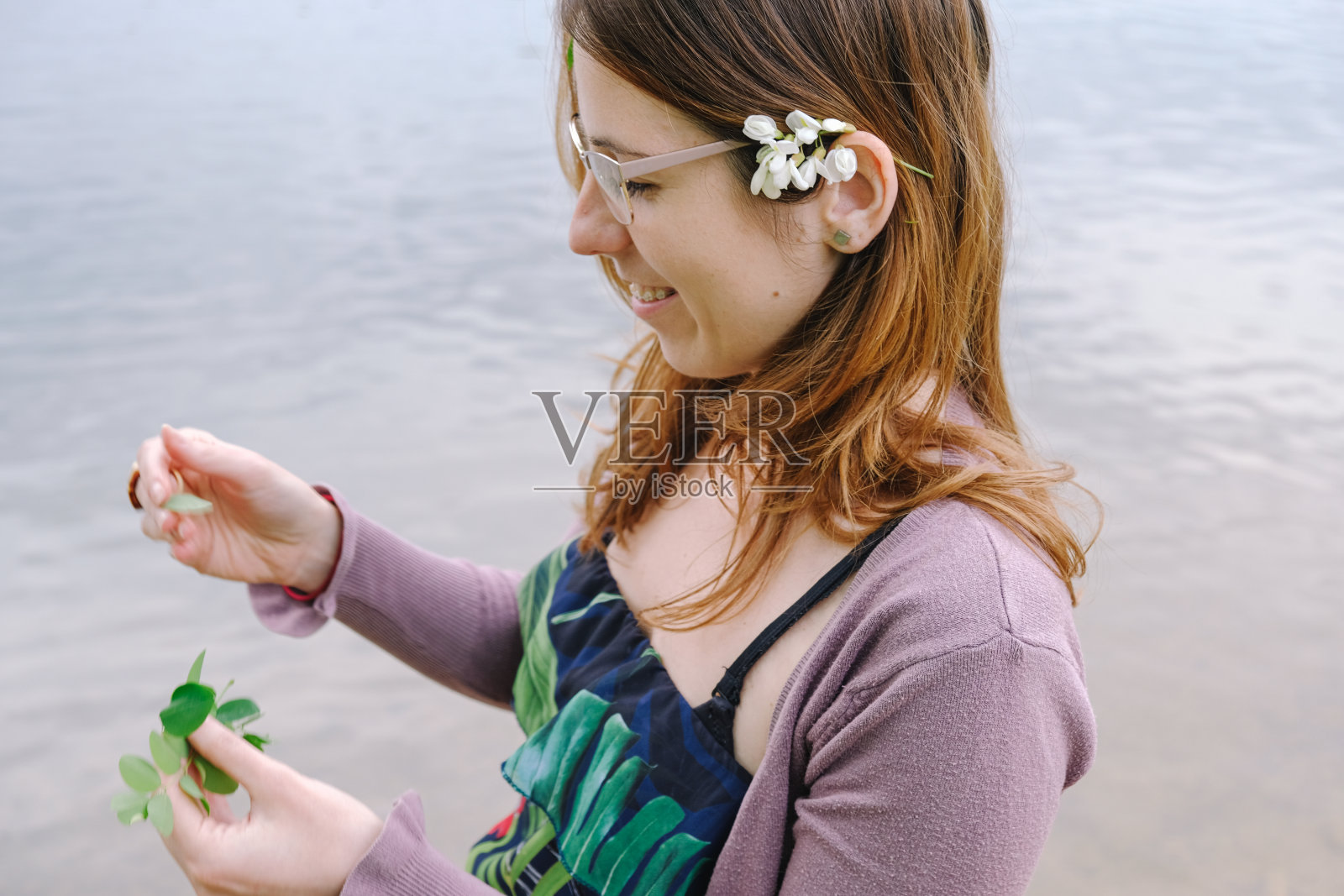 耳朵后面带着金合欢花的女人玩弄着植物的叶子照片摄影图片