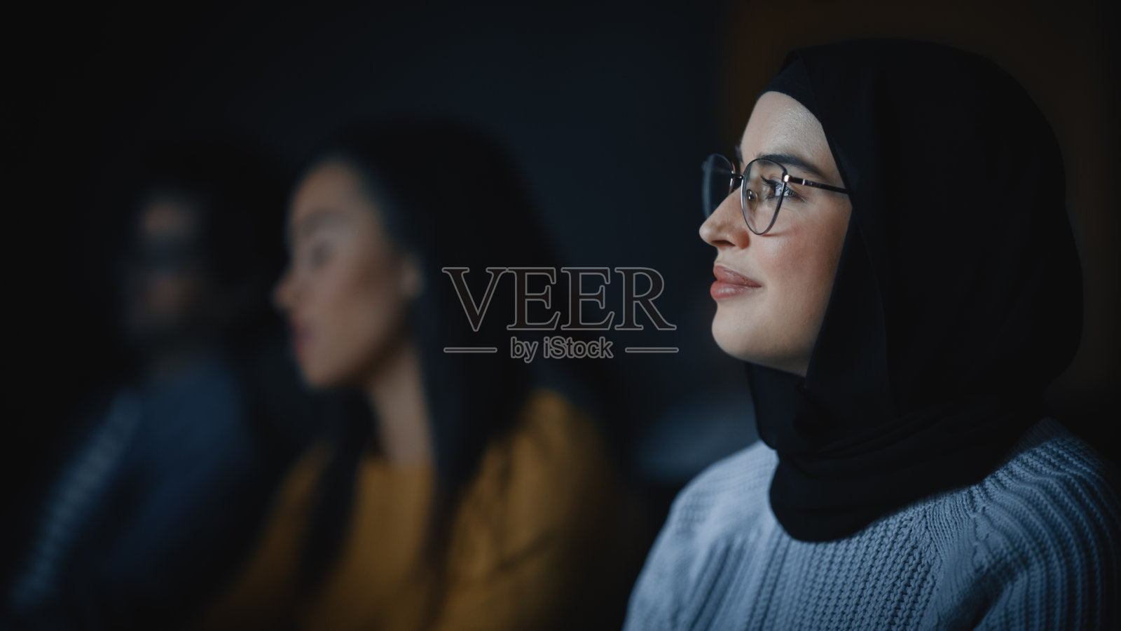 美丽的近距离肖像的一个多民族穆斯林女性戴着希贾布和眼镜，迷人的微笑和在相机摆姿势。快乐多样的年轻女子在休闲服装室内。照片摄影图片