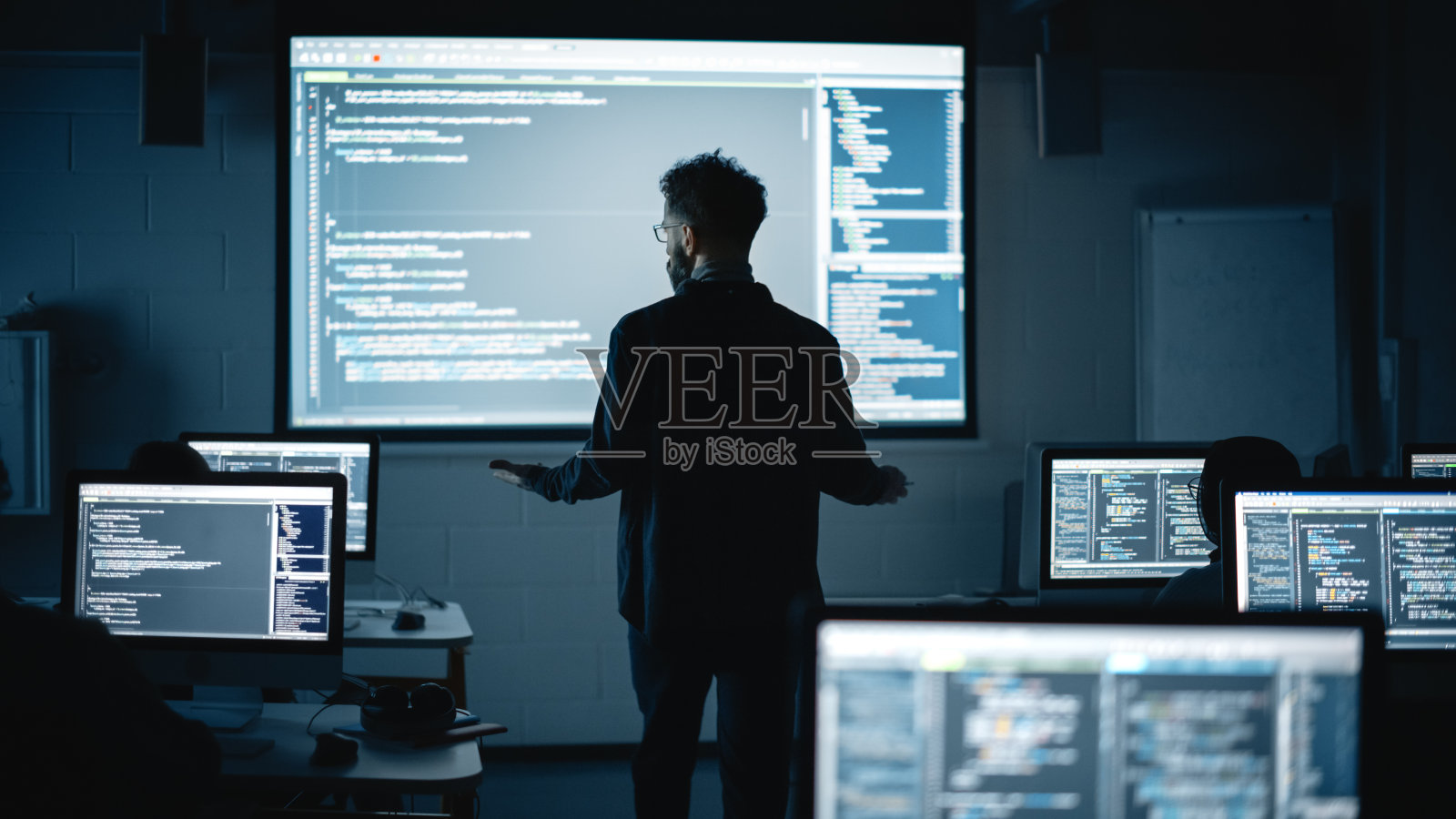 教师在黑暗的大学房间里给不同种族的男女学生讲授计算机科学。投影幻灯片与编程代码。解释信息技术。照片摄影图片