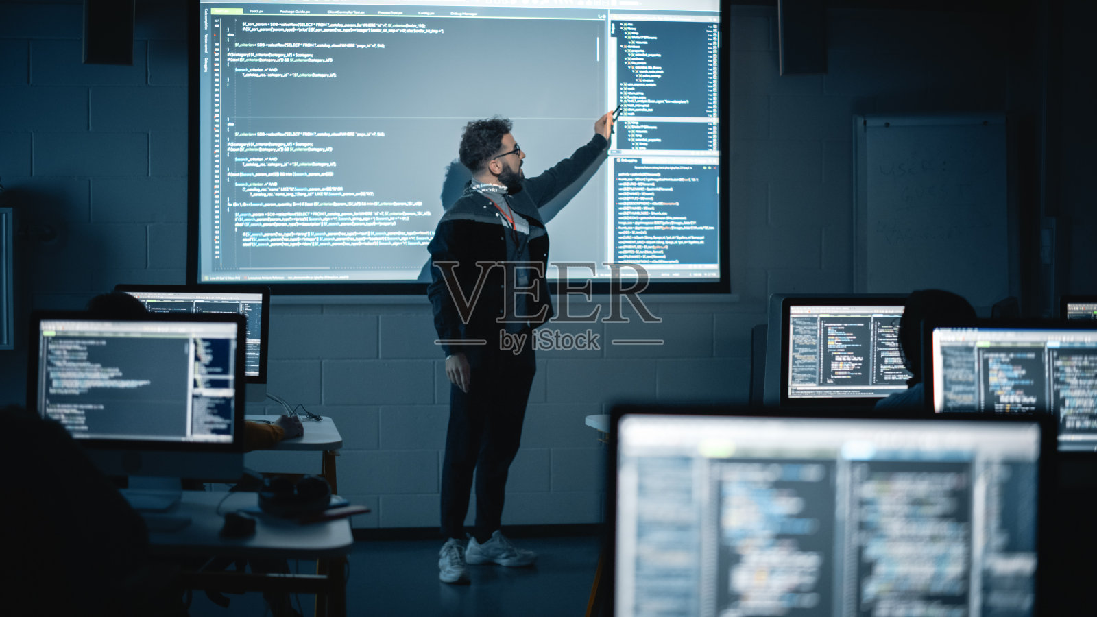 教师在黑暗的大学房间里给不同种族的男女学生讲授计算机科学。投影幻灯片与编程代码。解释信息技术。照片摄影图片