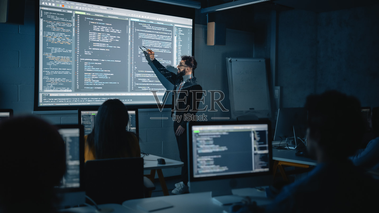 教师在黑暗的大学房间里给不同种族的男女学生讲授计算机科学。投影幻灯片与编程代码。解释信息技术。照片摄影图片