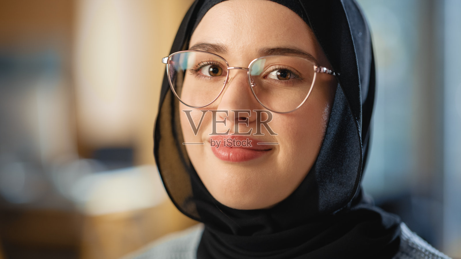 美丽的近距离肖像的一个多民族穆斯林女性戴着希贾布和眼镜，迷人的微笑和在相机摆姿势。快乐多样的年轻女子在休闲服装室内。照片摄影图片