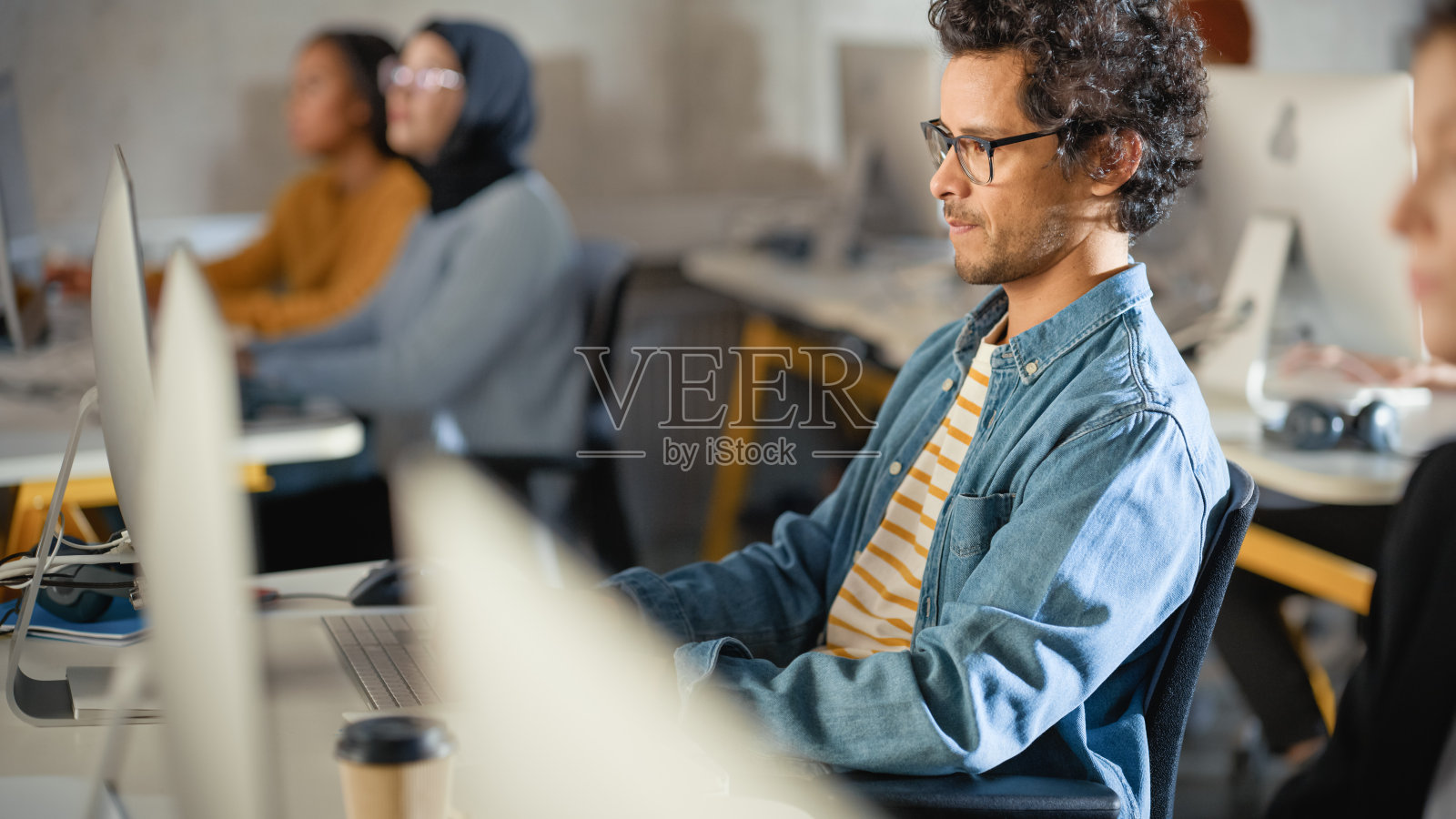 英俊聪明的男学生，在大学里与不同种族的同学一起学习。他在大学里研究台式电脑。在课堂上运用所学知识获取学术技能。照片摄影图片