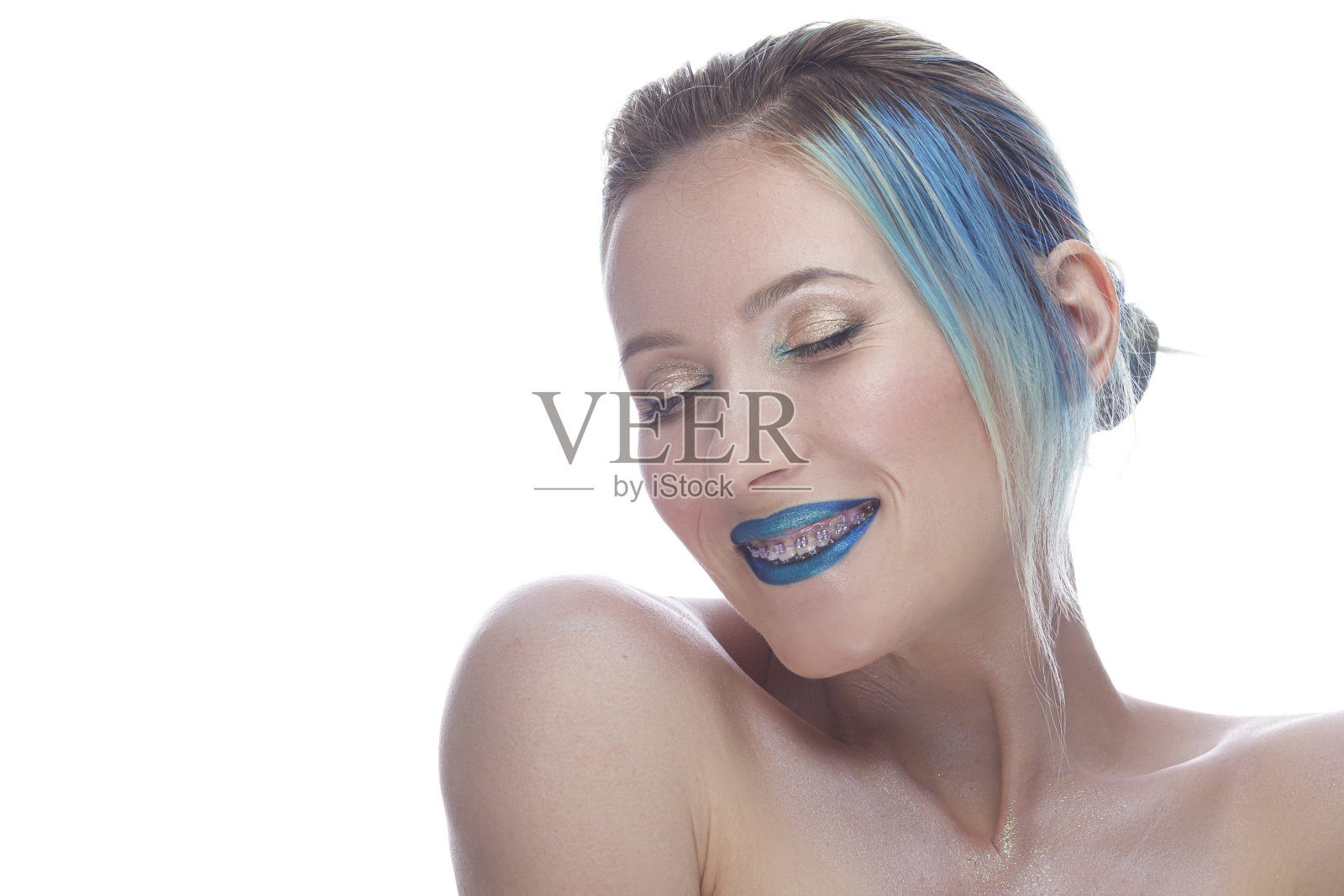 光滑和宁静的微笑年轻白人女性与丝般的皮肤和彩色的蓝色头发戴牙托在白色背景。照片摄影图片