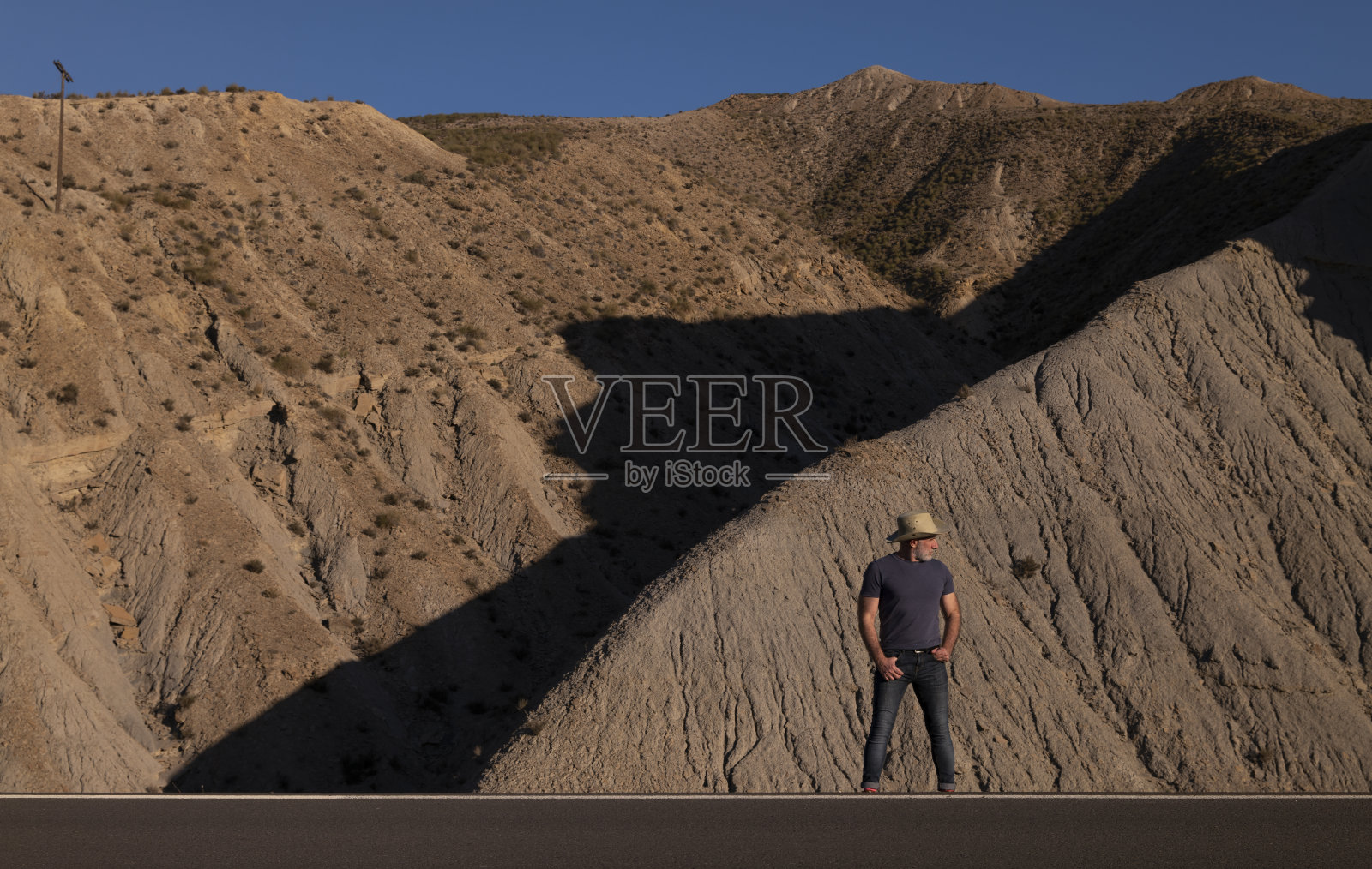 一个穿着牛仔的成年人在沙漠的路边对着山。西班牙阿尔梅里亚照片摄影图片