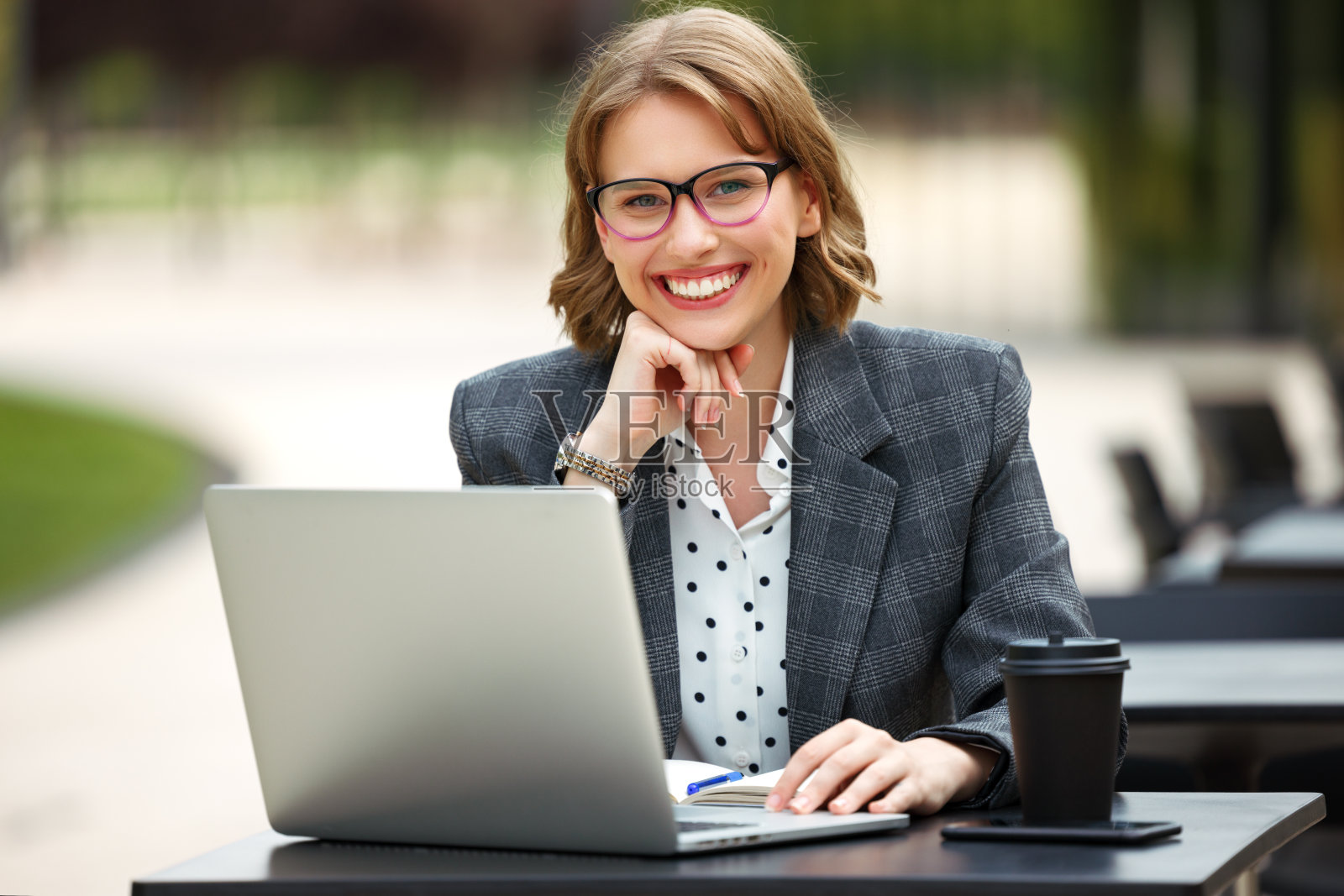 可爱的女商人，戴着眼镜，坐在外面拿着笔记本电脑和一杯外卖咖啡照片摄影图片