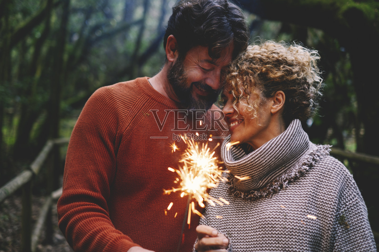 在森林绿树的背景下，一对浪漫的成年夫妇在火花的照耀下一起享受爱情。男人和女人用温柔和关系用火光和微笑庆祝照片摄影图片