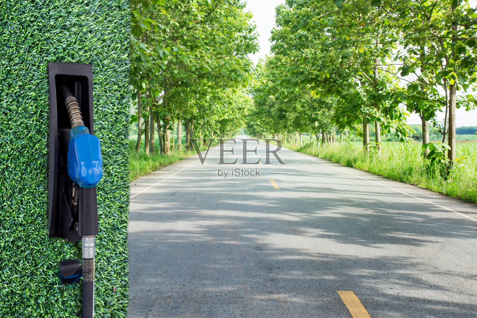 绿色的汽油喷嘴在道路两旁种植着行道树的背景。在白色背景下重新填充油气燃料。照片摄影图片
