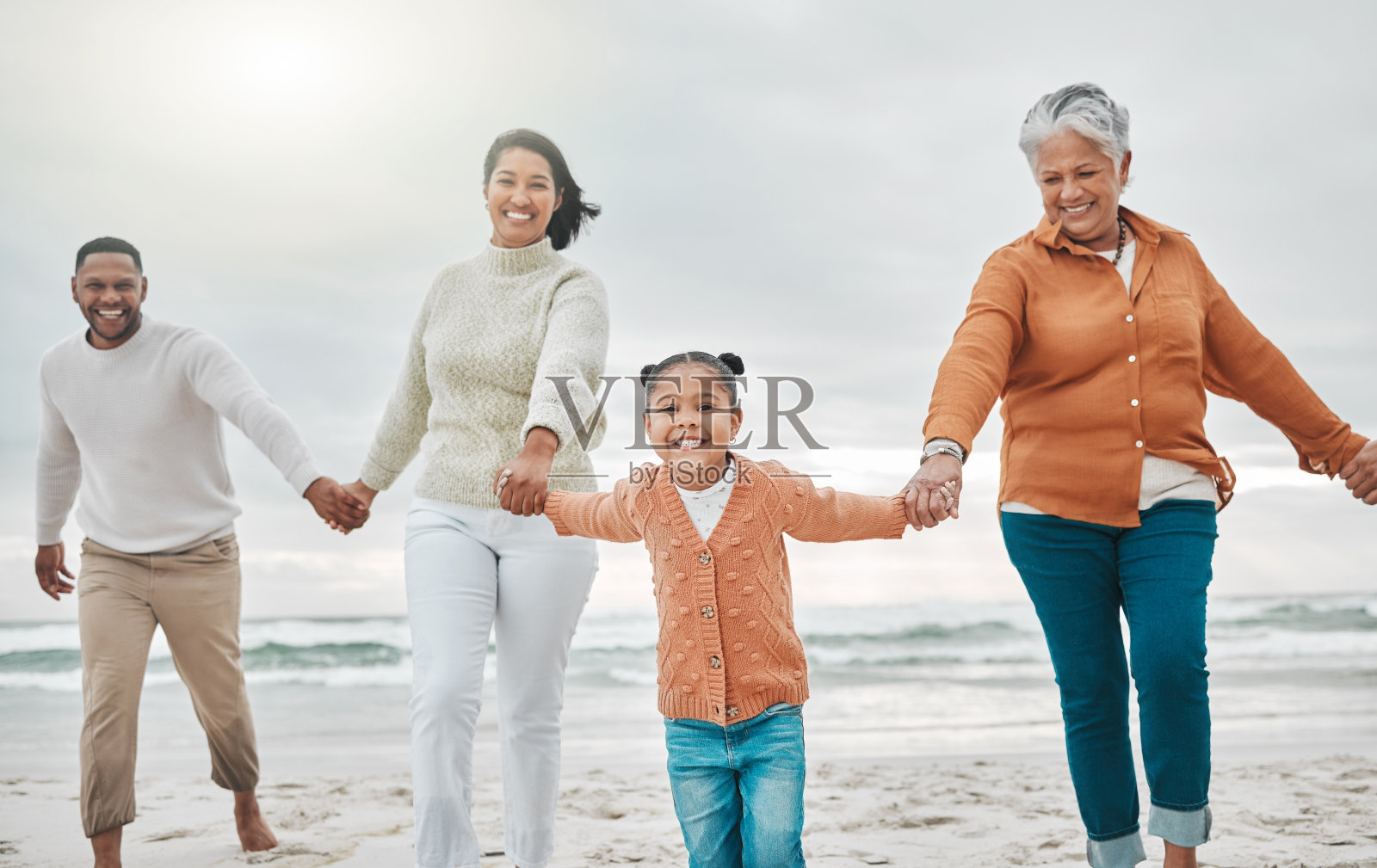 剪裁的照片，一个可爱的小女孩拉着她的父母和祖母沿着海滩照片摄影图片