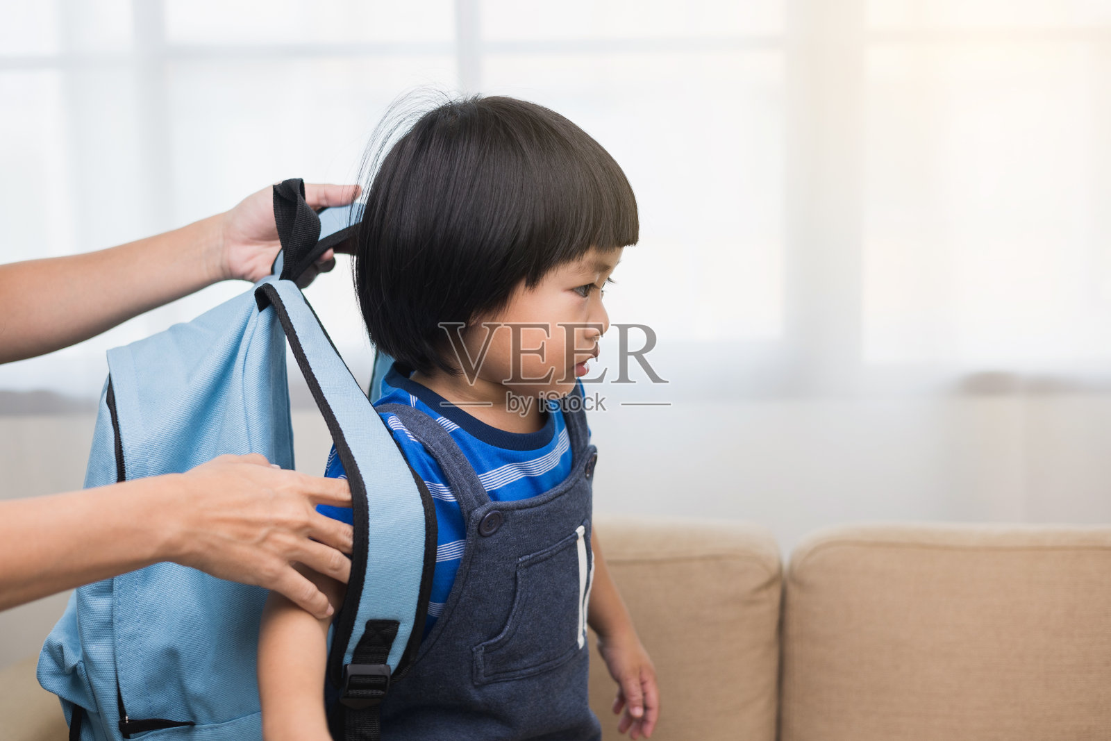 快乐的母亲谈话和说再见的小男孩带着书包在家里。第一天上学。回到学校概念。照片摄影图片