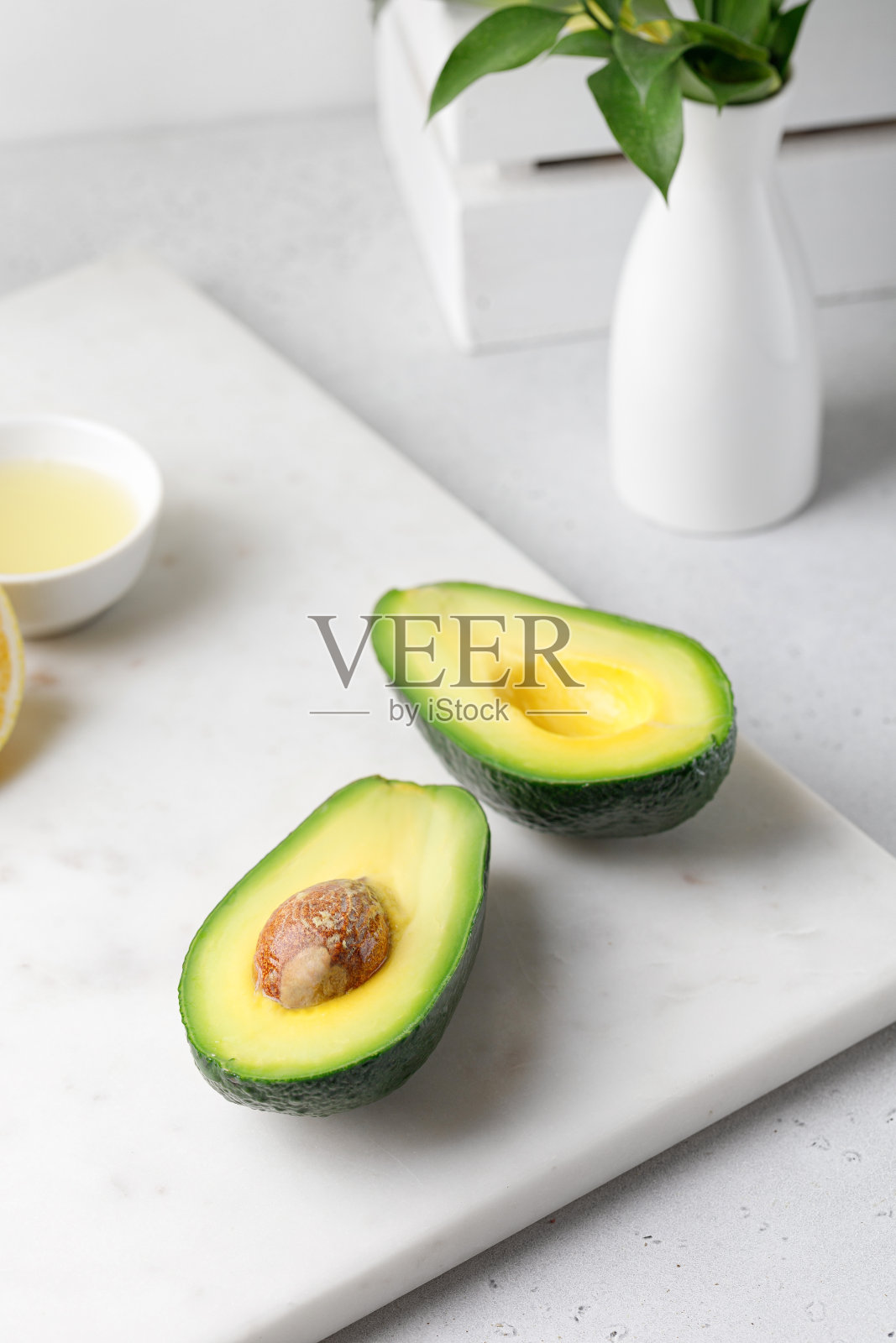 将成熟的绿色鳄梨切在白色大理石板上，配上花瓶和柠檬汁。食品成分。照片摄影图片