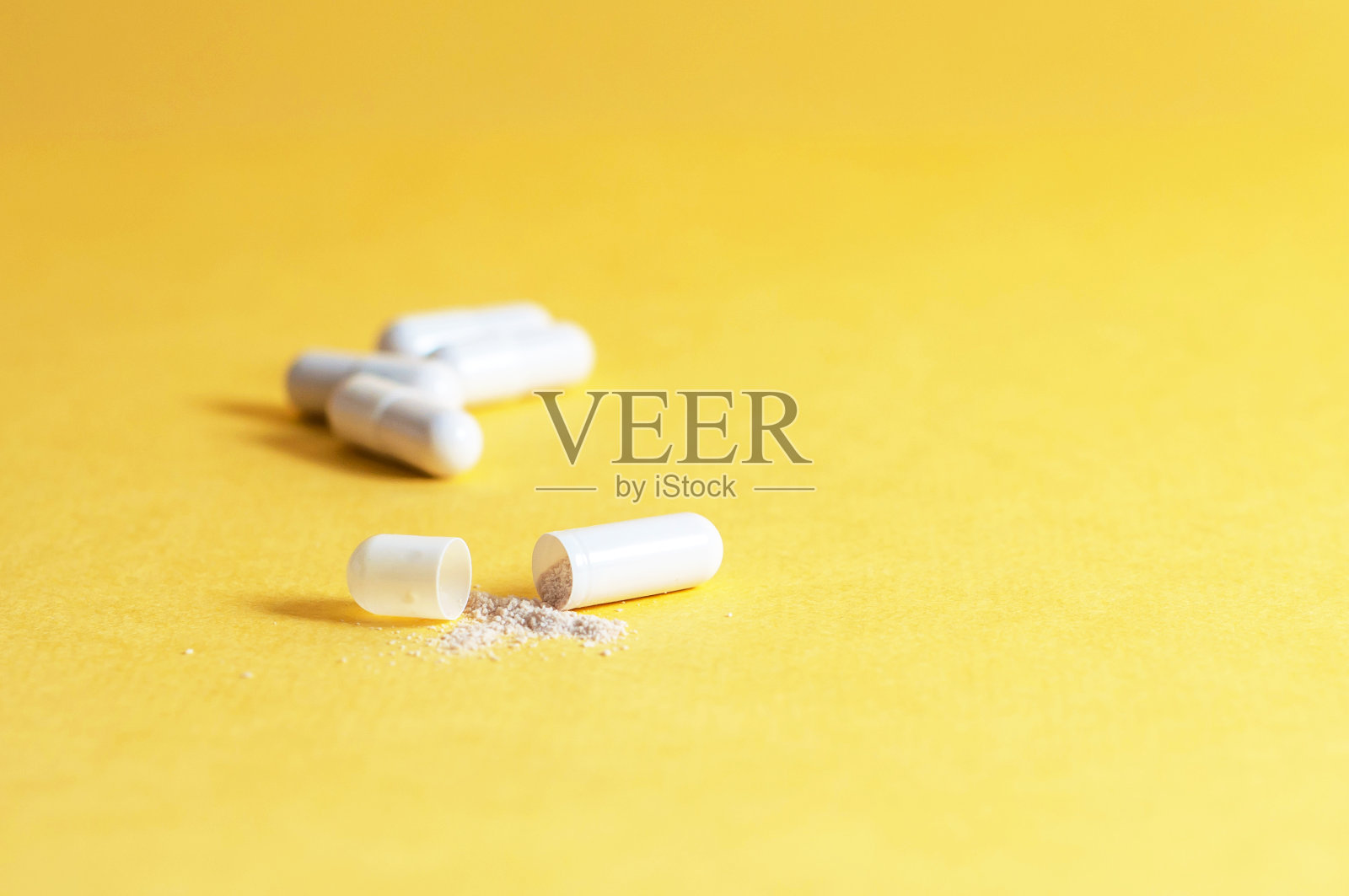 黄色的背景是胶囊，一个胶囊打开了，部分药物溢出来。副本的空间。照片摄影图片