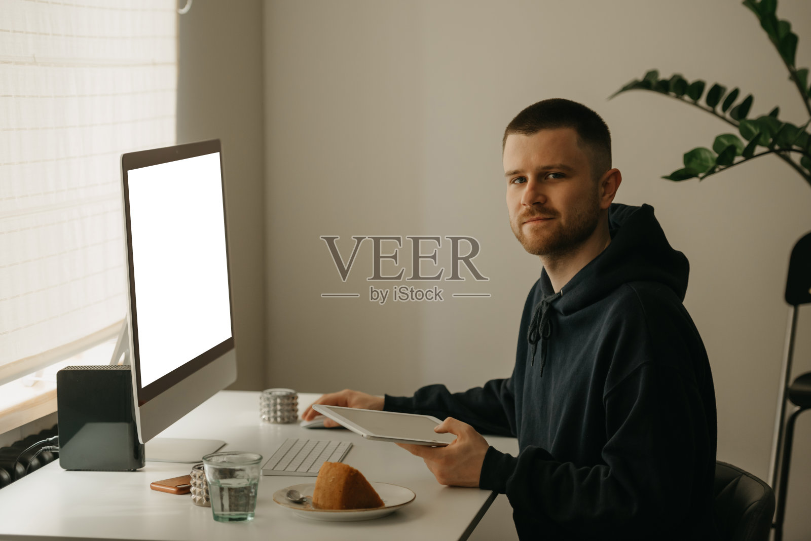 一名男子在家手持一台平板电脑，使用台式电脑远程工作。照片摄影图片