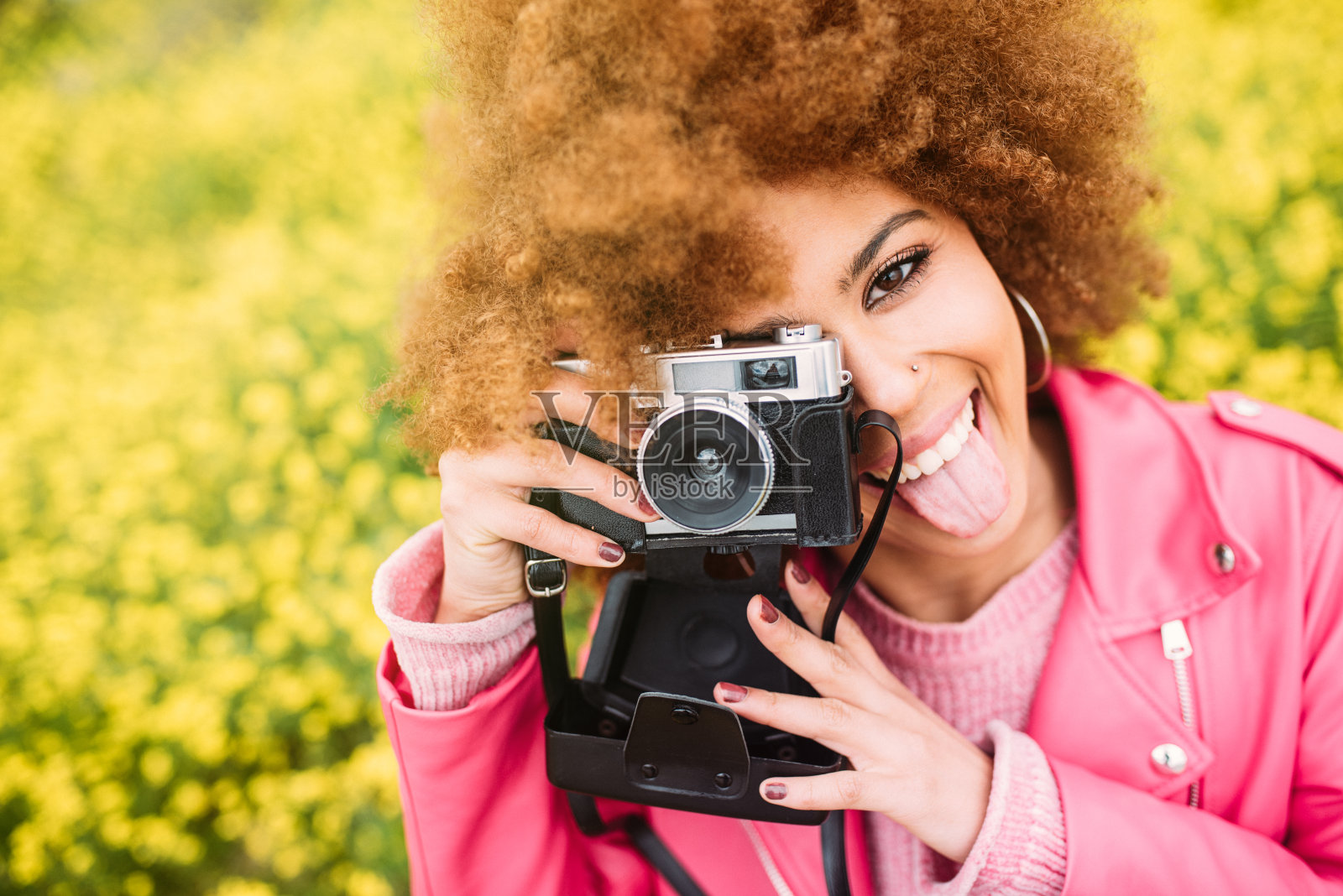 快乐的混血妇女在一个美丽的花田拿着一个老式相机照片摄影图片