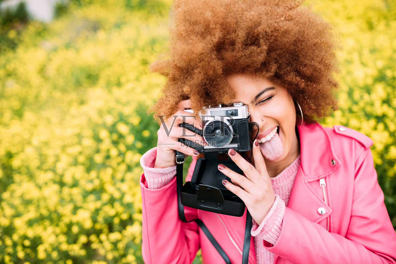 快乐的混血妇女在一个美丽的花田拿着一个老式相机照片摄影图片