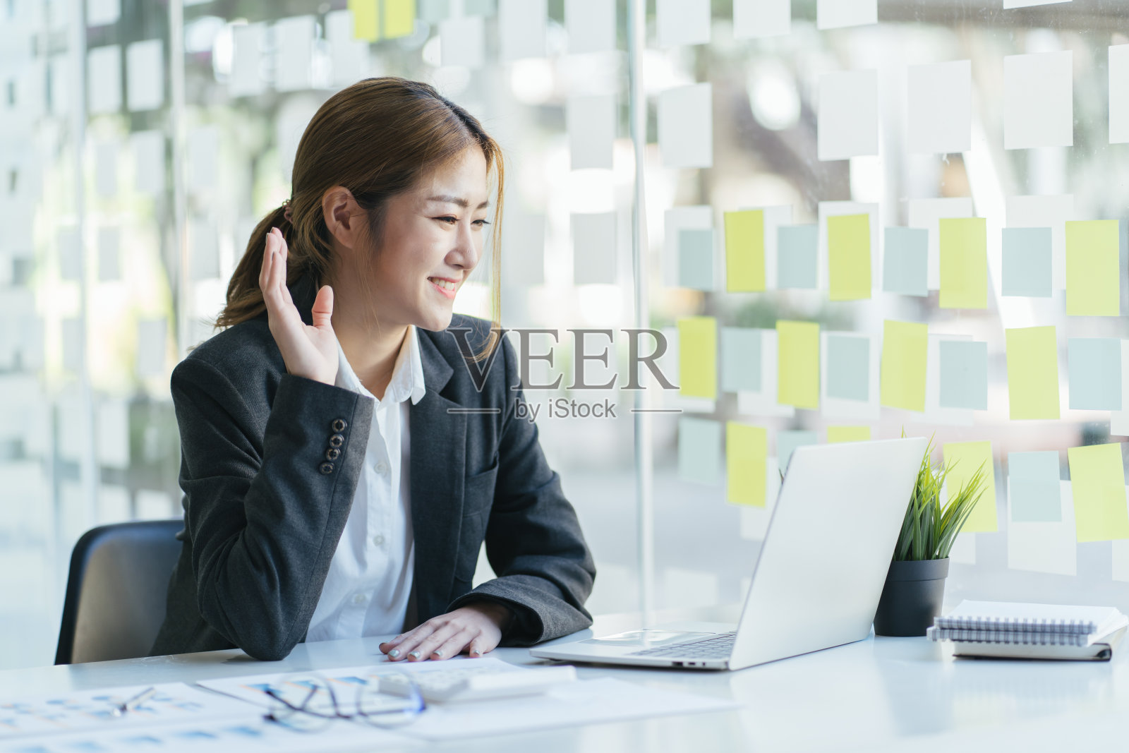 美丽积极的年轻女性享受在线交流的肖像，使用wifi与朋友视频会议，坐在打开的笔记本电脑前，微笑和挥手，说你好照片摄影图片