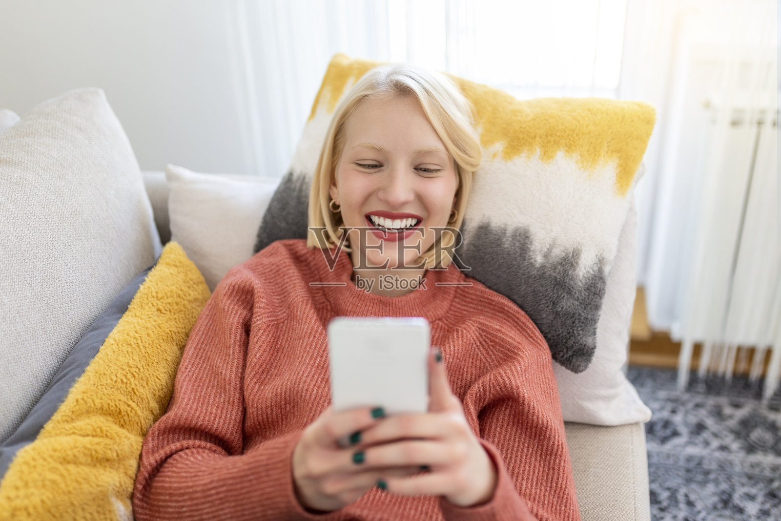 迷人的微笑女人坐在家里的沙发上用智能手机。沟通与舒适的理念。照片摄影图片