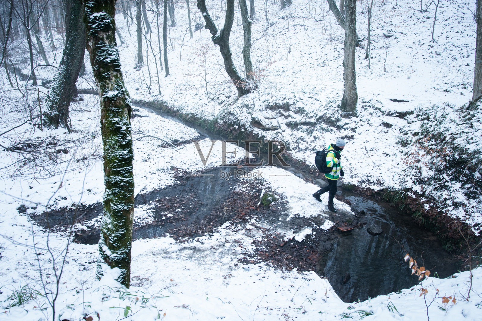 成年徒步旅行者在冬季森林接近水源。照片摄影图片