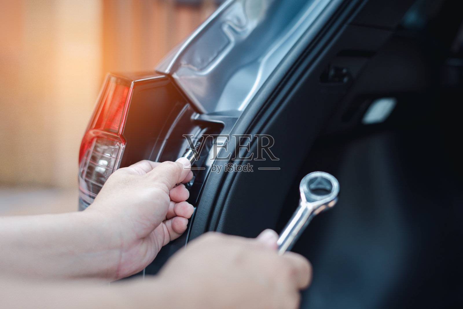 近手一名男子手持扳手与螺母块正拆卸汽车尾灯与车身照明系统的维护安全概念照片摄影图片