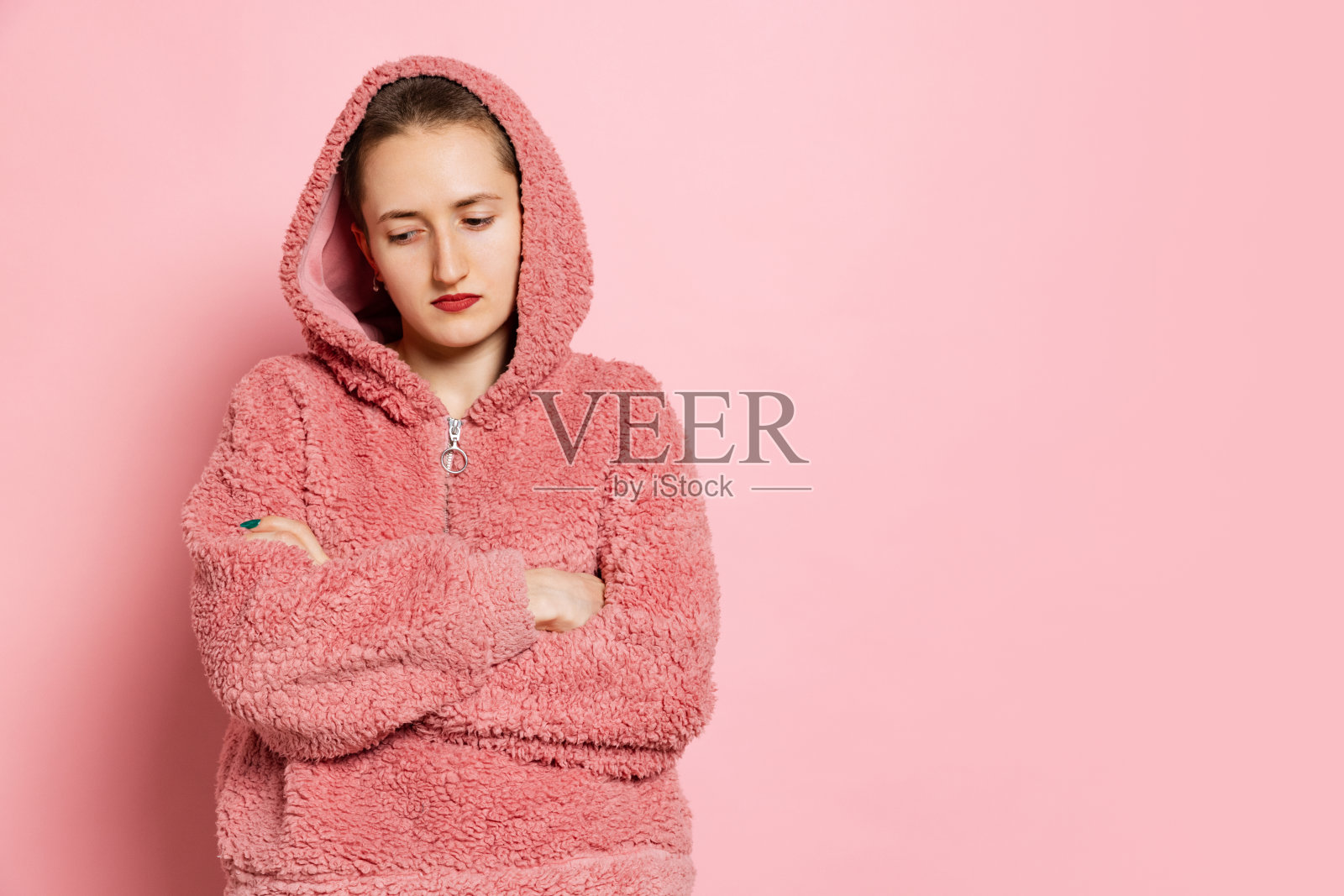 悲伤的年轻女子，留着短头发的学生，穿着粉红色的连帽衫，孤立在粉红色的背景上。情感概念，学习，广告照片摄影图片