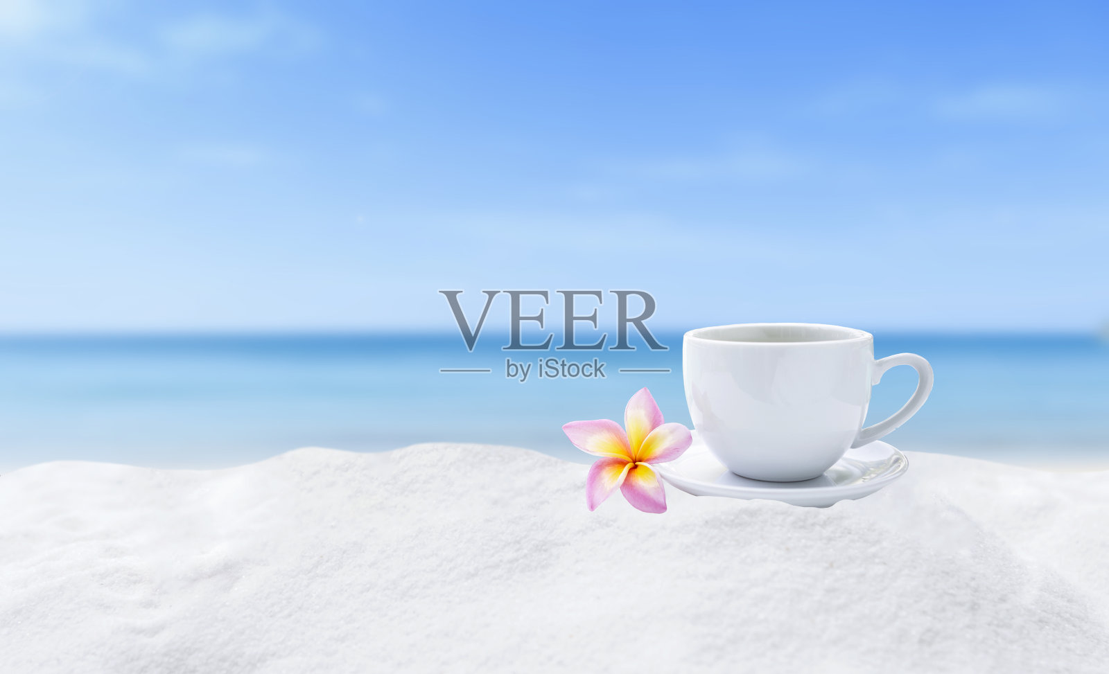 白色咖啡杯与鸡蛋花在白色的沙滩上模糊的背景照片摄影图片