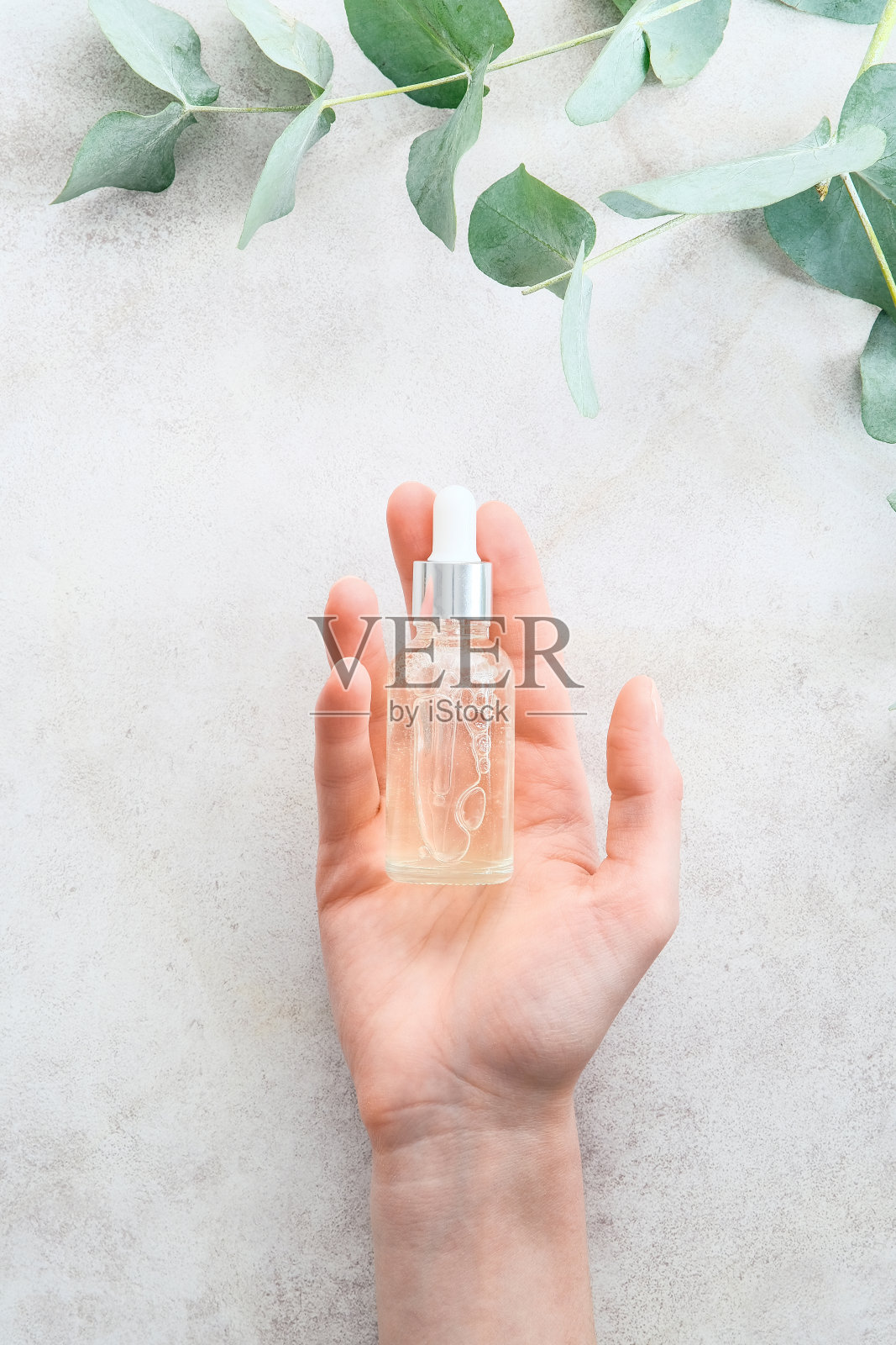 女性手拿透明滴管瓶，在大理石桌子上涂满乳液。护肤化妆品概念。照片摄影图片