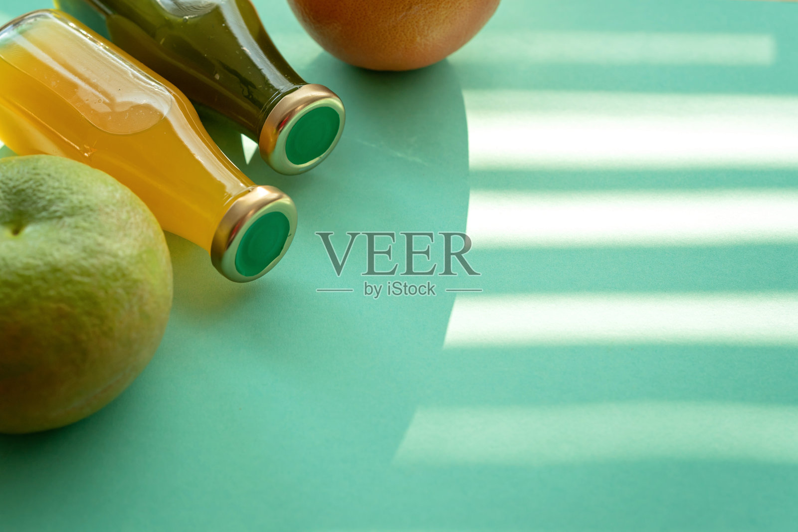 水果和装有果汁和冰沙的玻璃瓶放在薄荷色的背景上。不同的柑橘类水果:葡萄柚、甜橙和玻璃瓶里的鲜榨果汁照片摄影图片