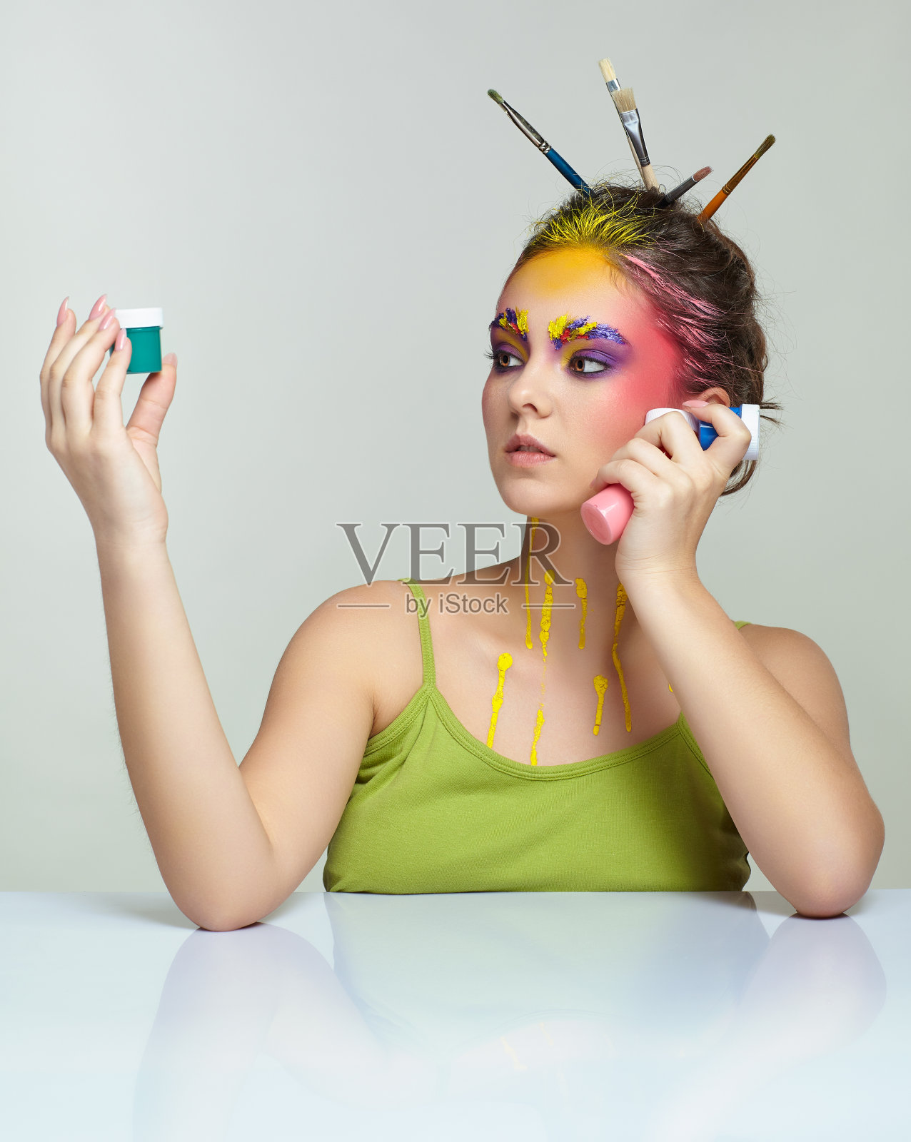 一名年轻女子的肖像，在桌子前摆姿势，头发上插着画笔，手里拿着水粉画。照片摄影图片