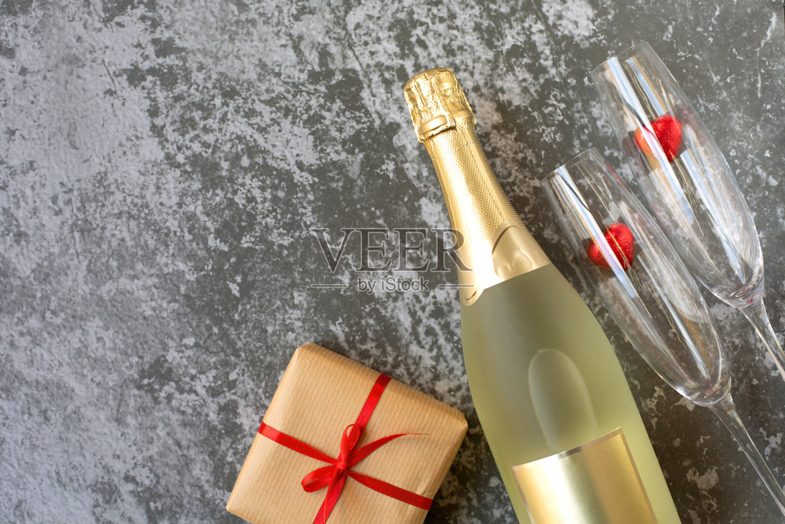灰色的背景上是一瓶香槟、两个玻璃杯和一份用红丝带纸包着的情人节礼物。照片摄影图片
