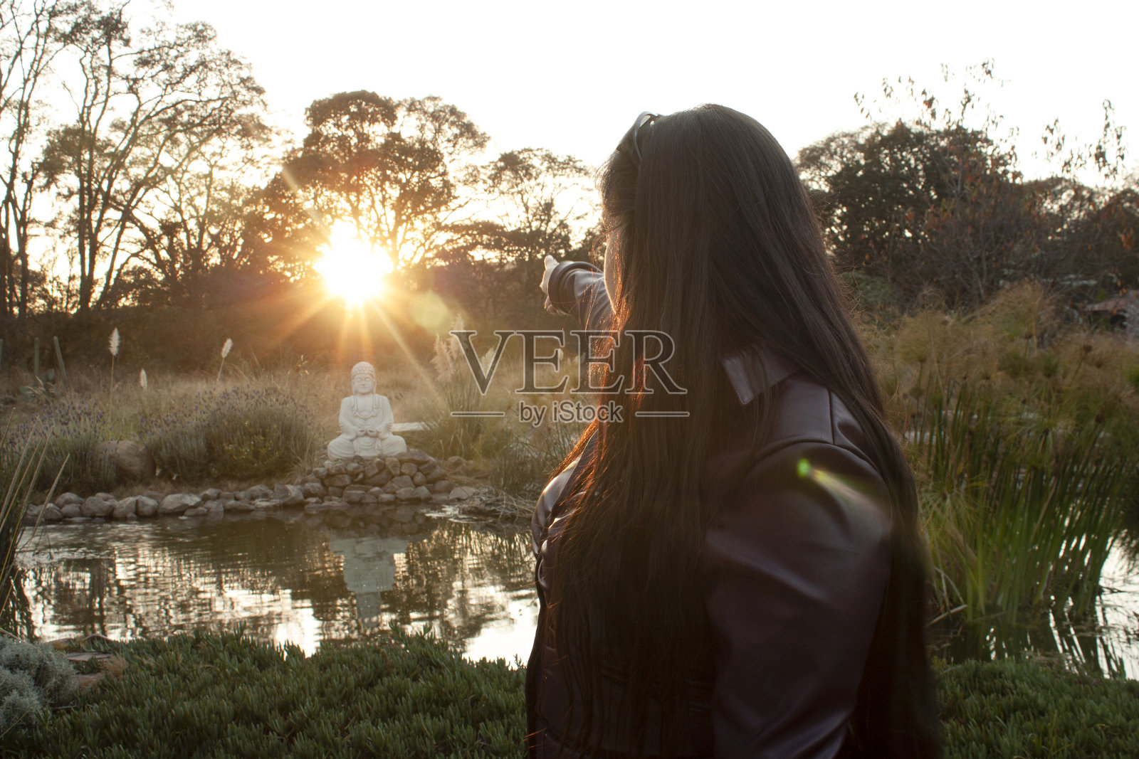 身着紫色皮夹克的女子将手指向夕阳下照亮佛像的金色太阳照片摄影图片