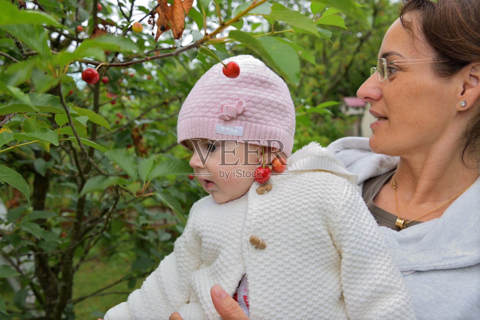 一个耳朵上挂着红樱桃的孩子抓着甜美成熟的樱桃照片摄影图片