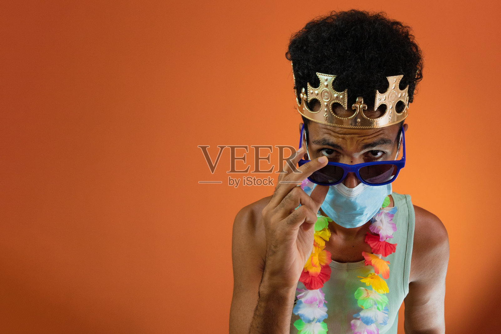 身着狂欢节服装，戴着大流行口罩的黑人男子被隔离在橙色背景下。照片摄影图片