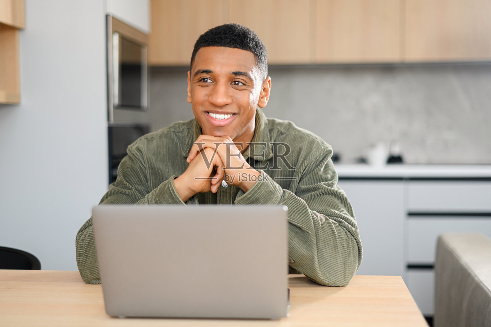 乐观的多种族男性自由职业者，在笔记本电脑显示器前看向别处。学生坐在书桌前上网照片摄影图片