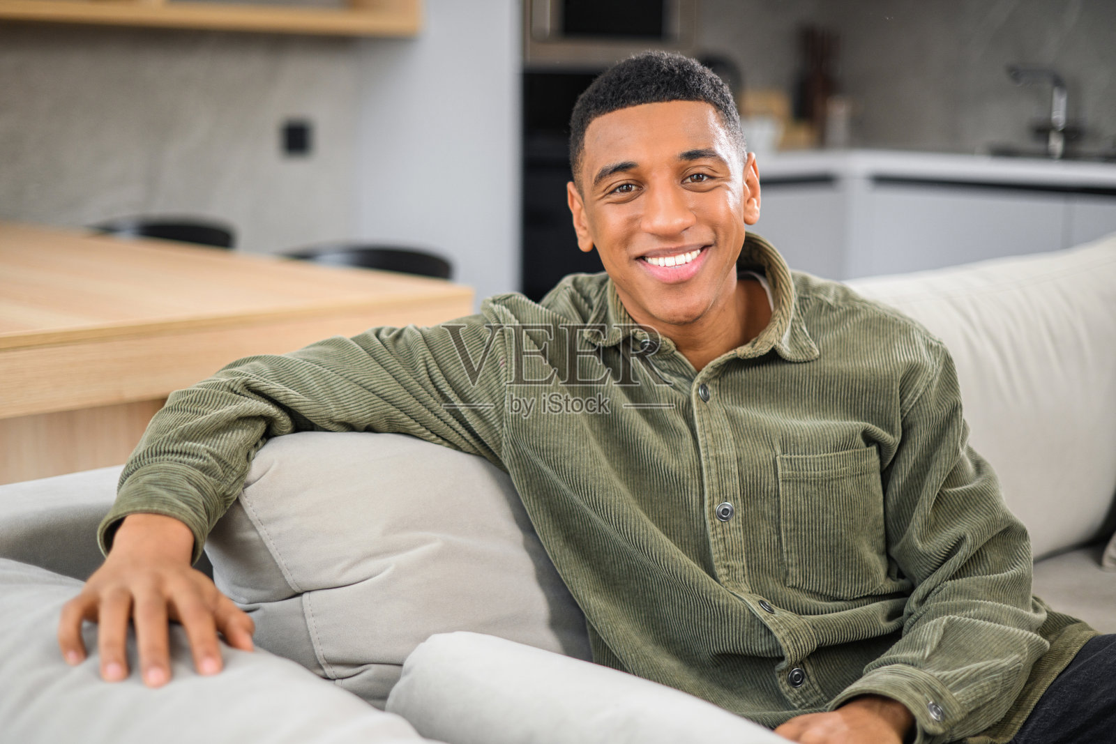 民族男子坐在沙发上微笑，同时感到舒适和放松。背景是厨房。休闲的生活方式照片摄影图片
