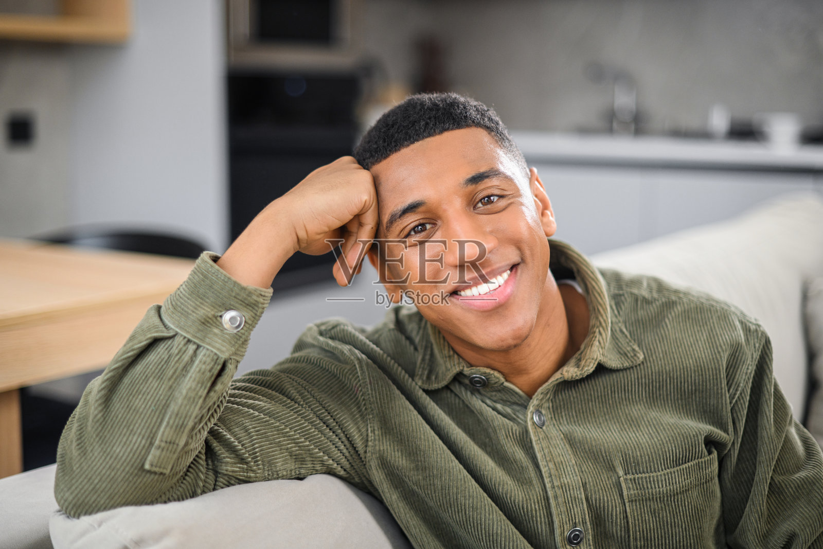 一幅年轻俊男在现代家居客厅休息的画像，随意坐在沙发上，看着镜头，心情轻松照片摄影图片