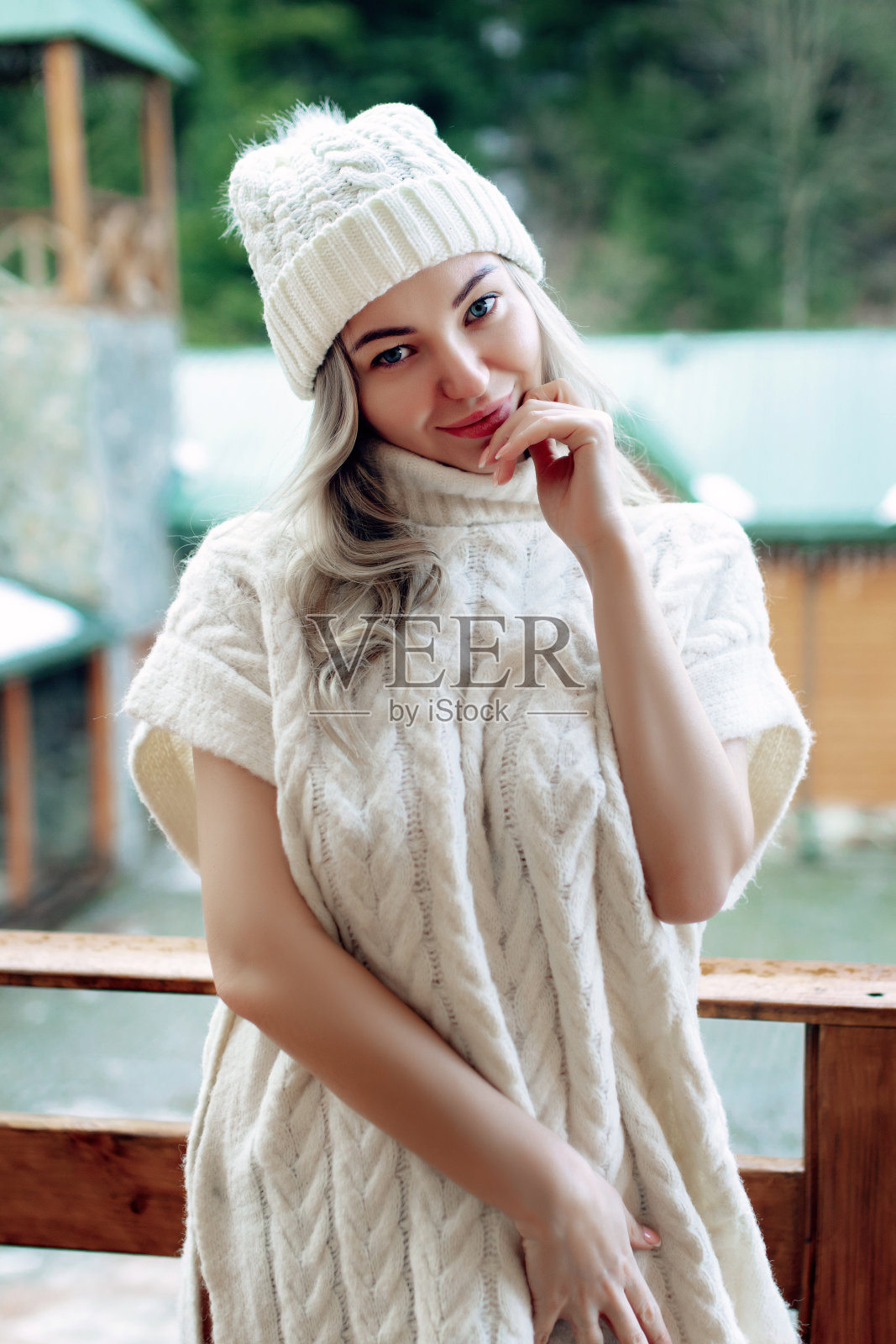 一个漂亮的女孩戴着白色的帽子和毛衣在阳台上的街道上的肖像。温暖的冬天的衣服照片摄影图片