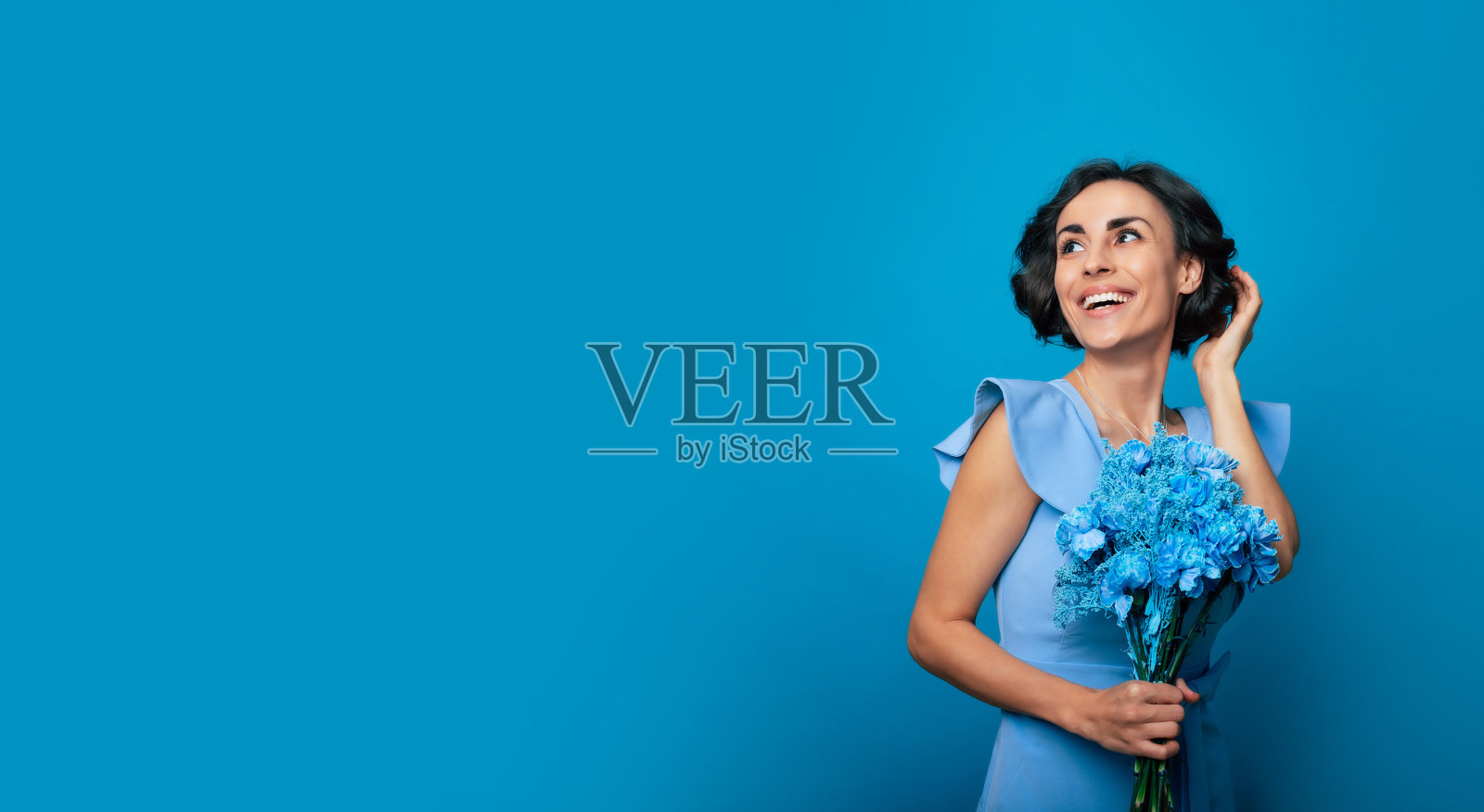 一位身穿蓝色礼服的快乐年轻女子手捧鲜花摆姿势，庆祝母亲节和妇女节，迎接春天照片摄影图片